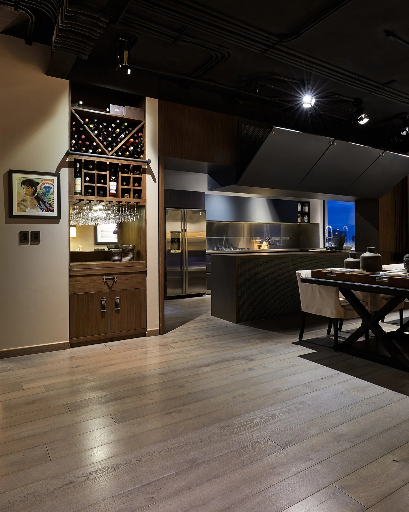 Cocina moderna con paredes de madera, estantes con botellas de vino y copas, alguna obra de arte en la pared, y mesa de comedor.