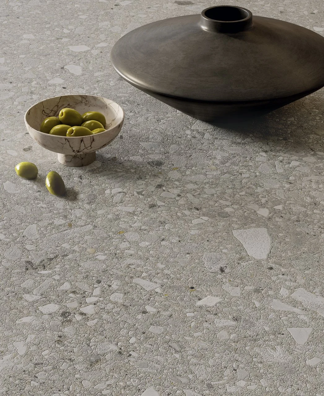 Una bola de cristal con aceitunas verdes y una bandeja grande de cerámica en una superficie de piedra.