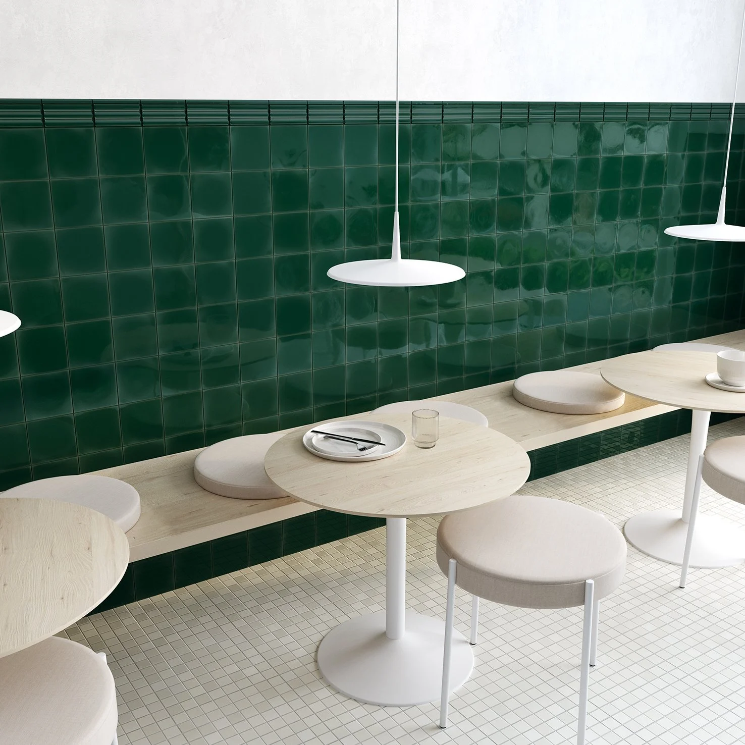 Mesas y sillas en un restaurante con pared de azulejos verdes y lámparas blancas suspendidas.