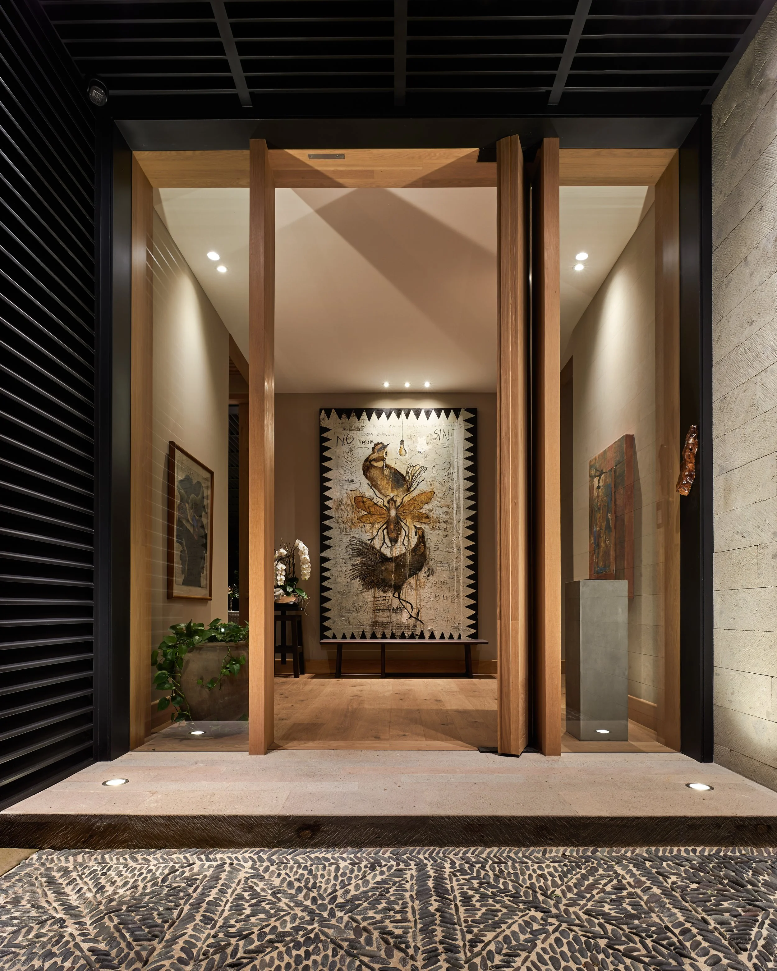Entrada a una sala de arte con puertas de madera y paredes decoradas con cuadros, incluyendo una obra central con una imagen de una mariposa y objetos decorativos.
