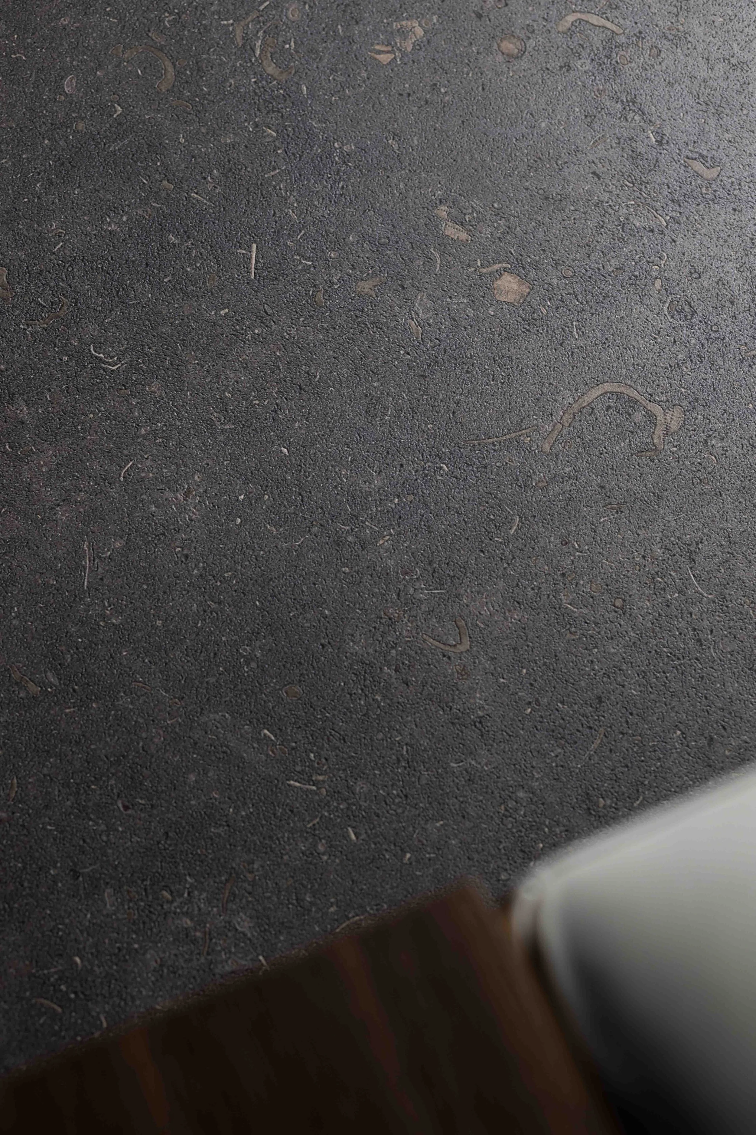 Superficie oscura con textura áspera, con pequeños pedazos de basura y una esquina en la parte inferior derecha.