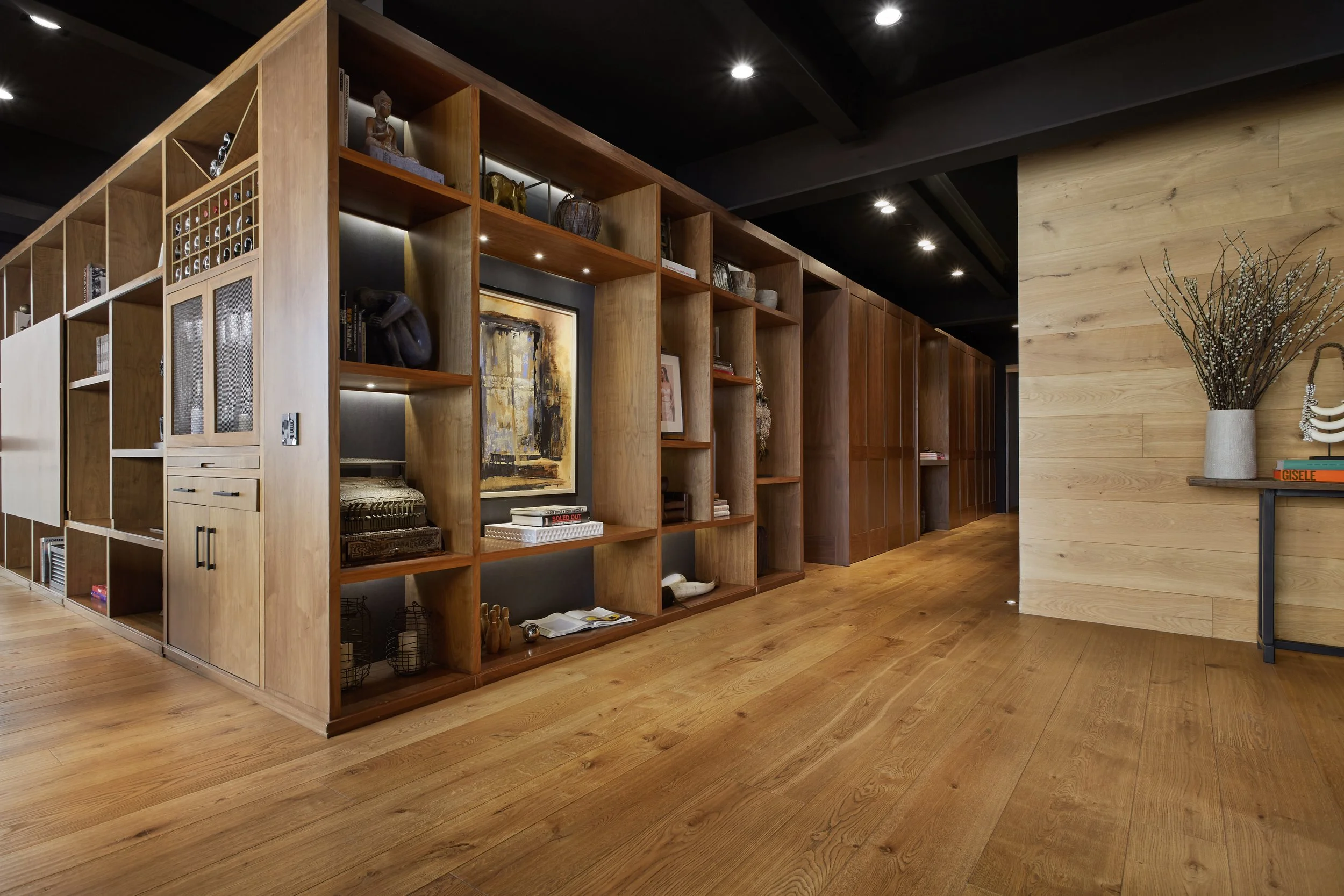 Estantería de madera con objetos decorativos, libros y arte en una sala de diseño moderno con paredes de madera y suelo de madera.
