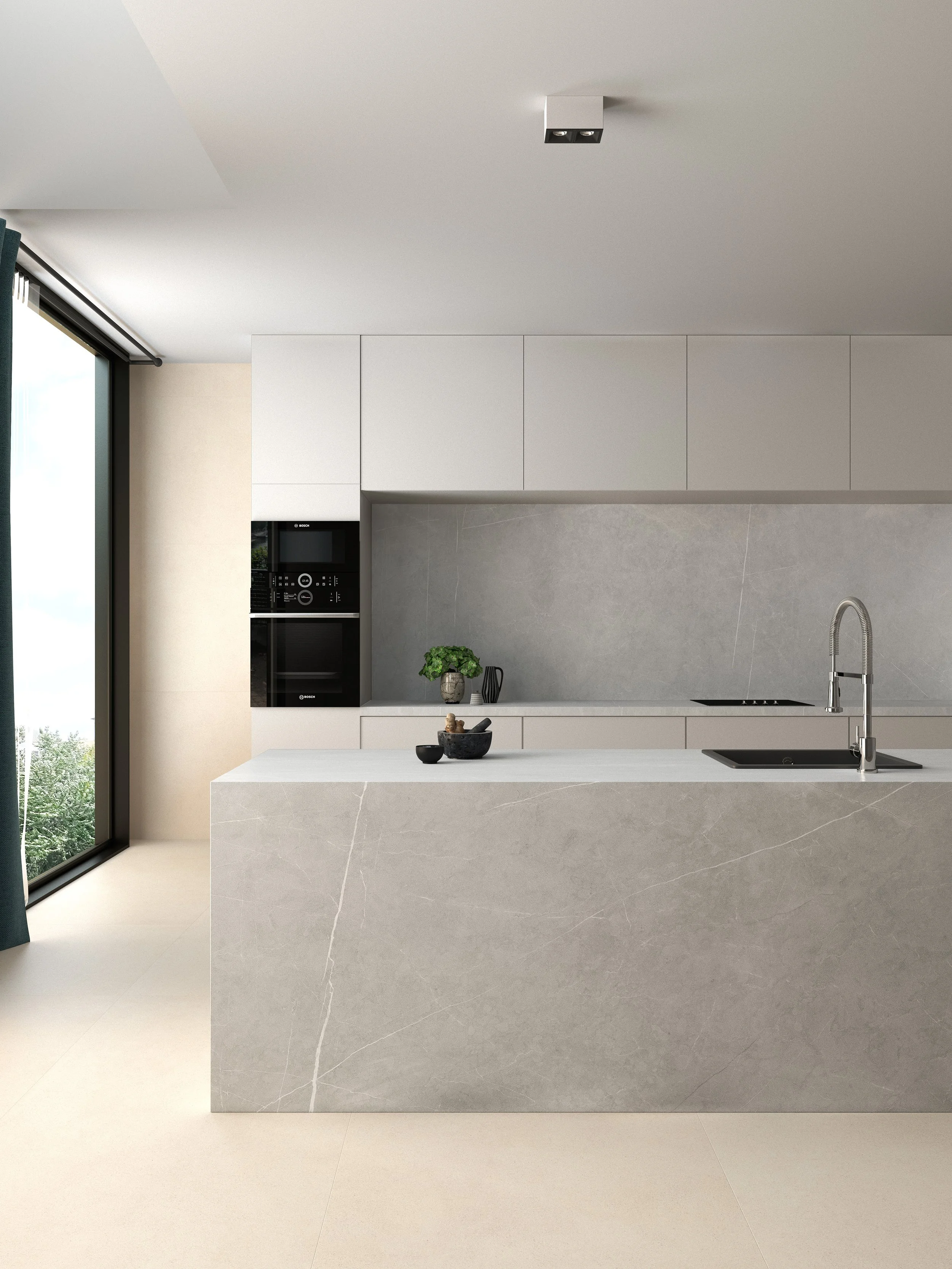 Cocina moderna con encimera de piedra beige y electrodomésticos negros integrados, ventanas grandes con cortinas oscuras y decoraciones minimalistas.