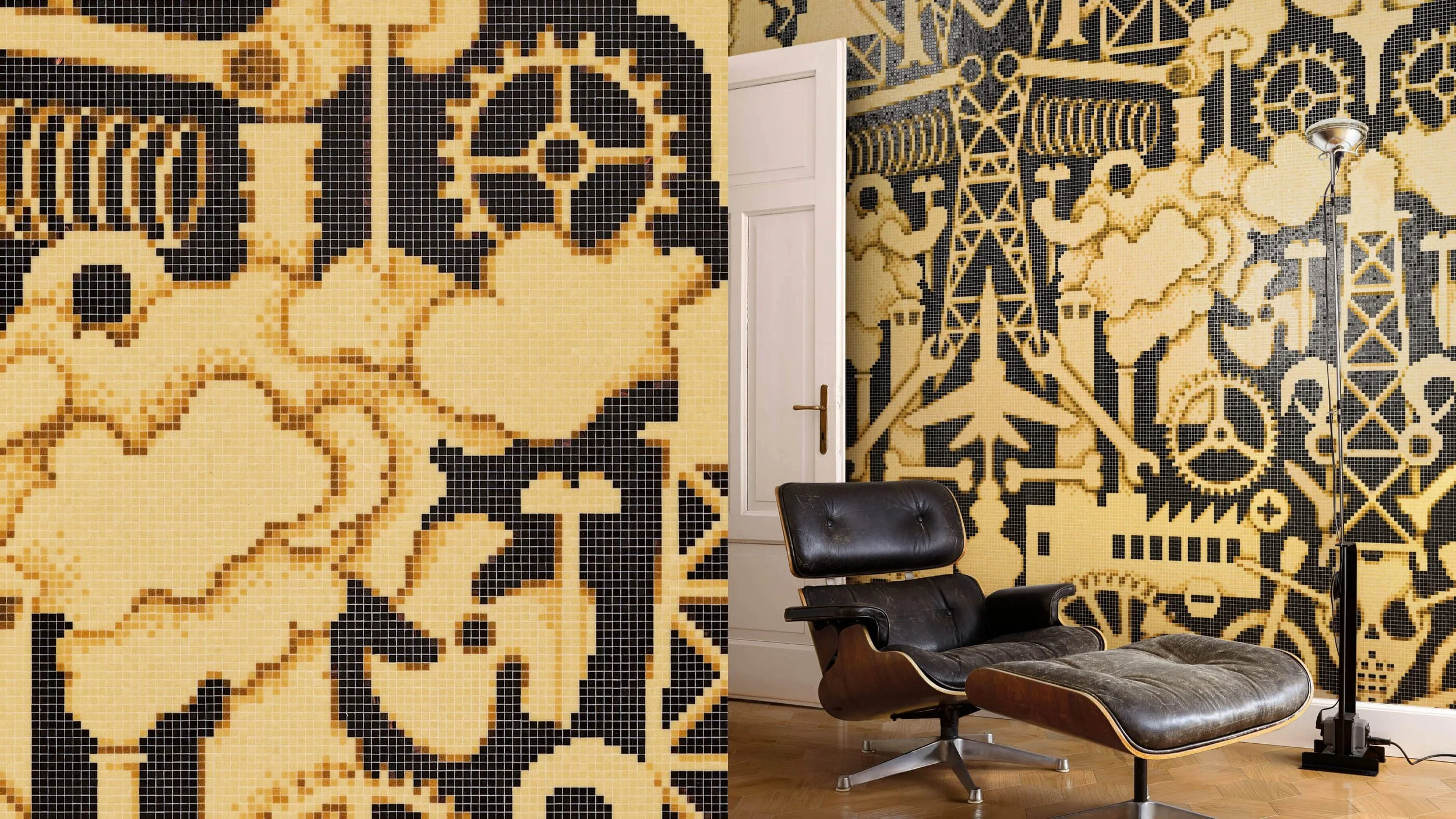 Sala con paredes decoradas con mosaicos en tonos beige y negro, sillón negro estilo Eames con otomana y lámpara de piso