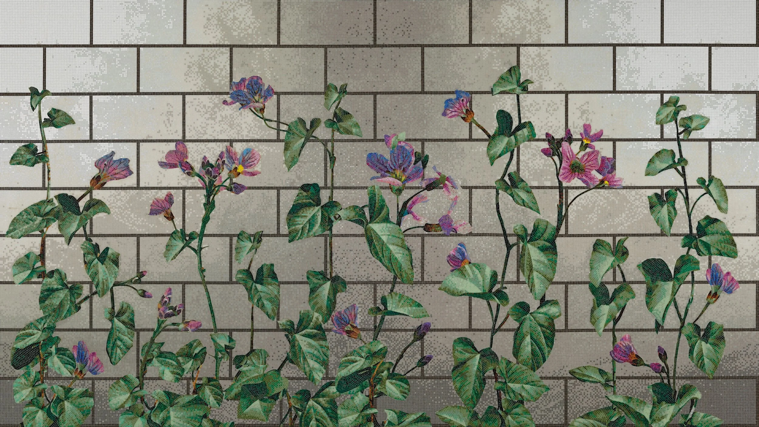 Mosaico de flores moradas y verdes contra una pared de ladrillos blanca.