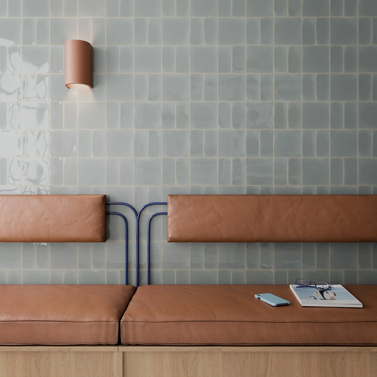 Bancada de espera con cojines de cuero, una lámpara de pared y algunas pertenencias como gafas, teléfono móvil y revista sobre el asiento.