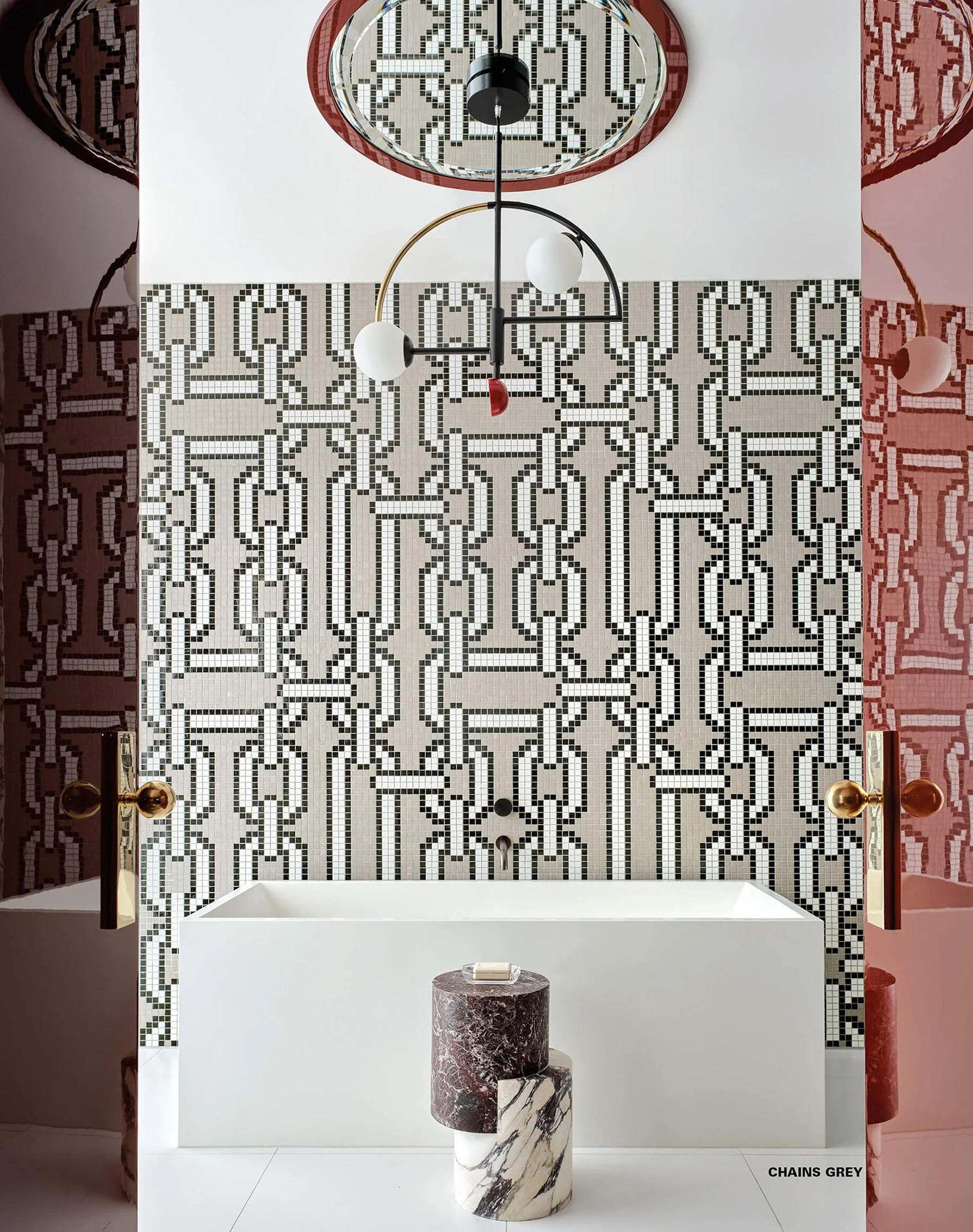 Baño moderno con pared de mosaico en tonos blancos y negros, bañera blanca, espejo de techo redondo con mosaico, lámpara moderna, puertas con pomos dorados y un soporte de mármol color vino y mármol blanco.