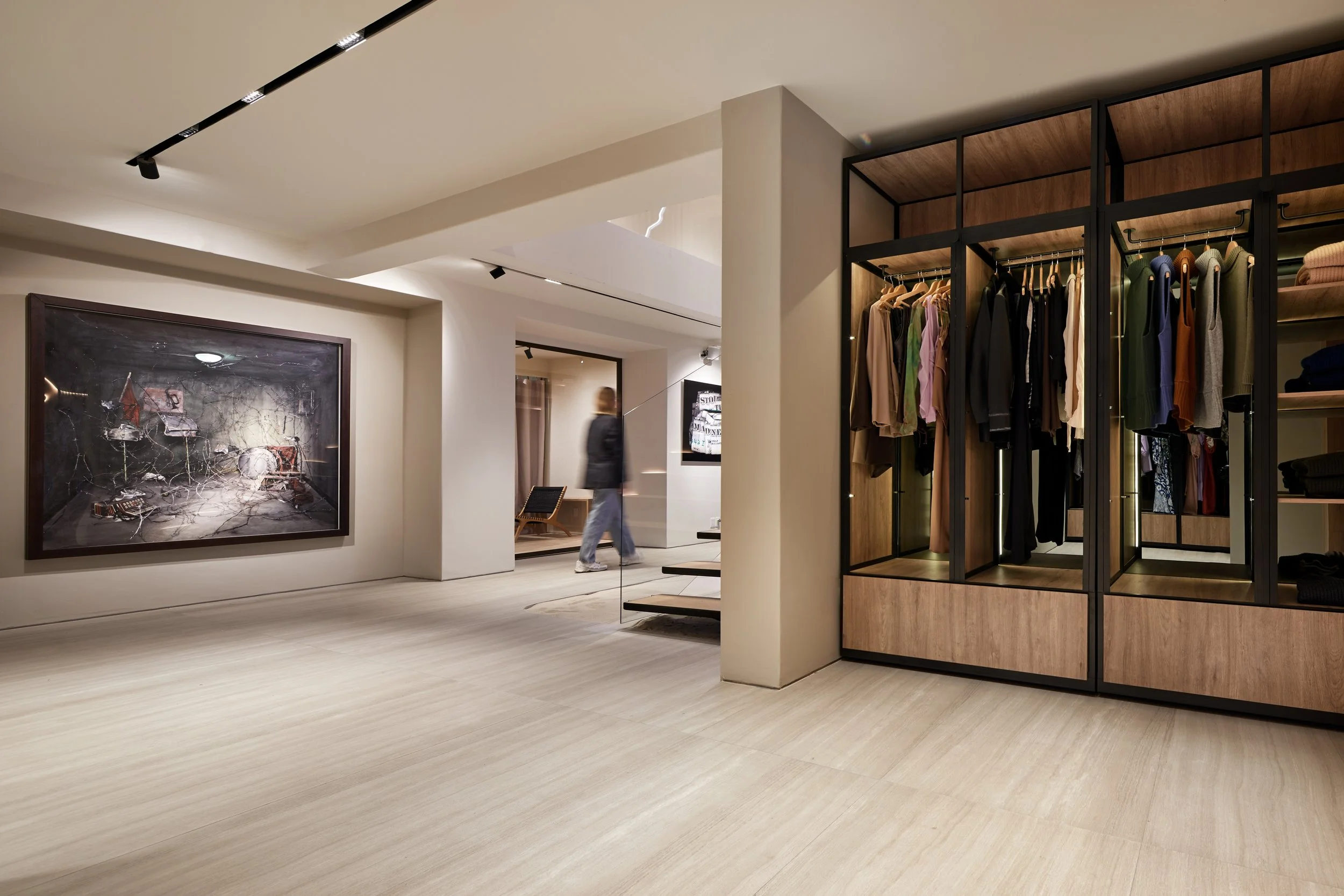 Interior de una tienda de ropa moderna con exhibidores de ropa, una pintura en la pared y un cliente paseando.