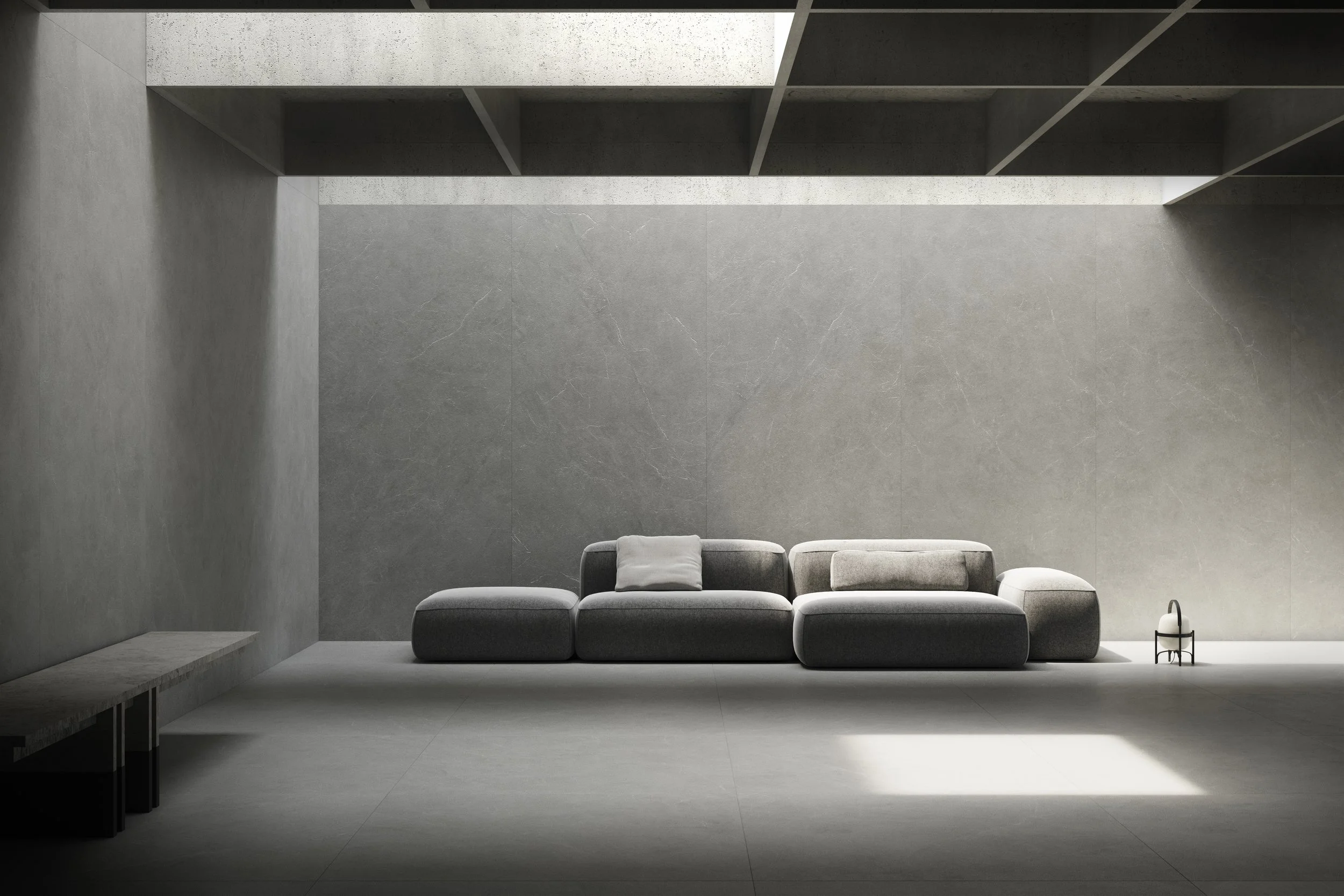 Sala moderna y minimalista con sofá gris, cojines y pequeña mesa decorativa, iluminada por luz natural