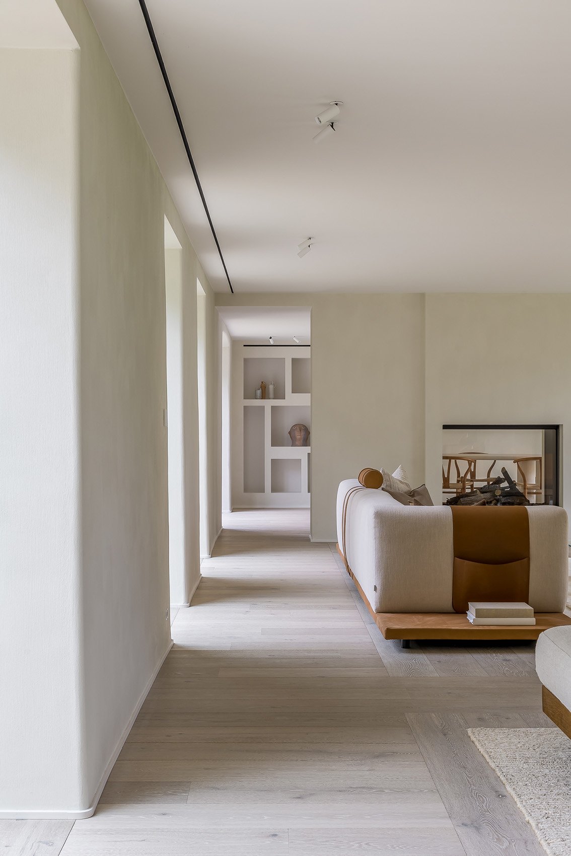 Interior moderno de sala con sofá beige, chimenea y estantería decorativa, luz natural