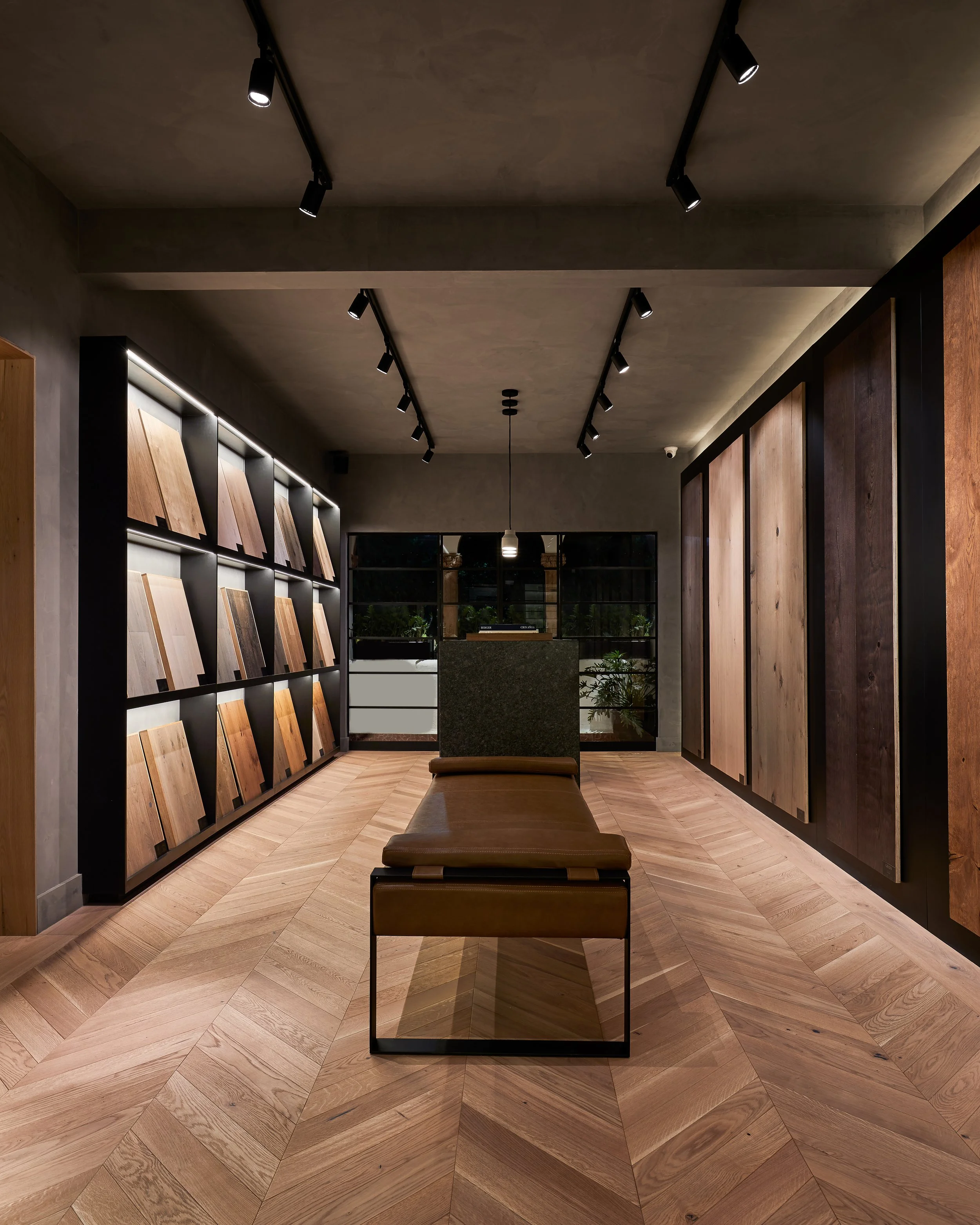 Galería de exhibición de tablas de madera decorativas en una tienda, con banco de cuero en el centro y luces dirigidas.