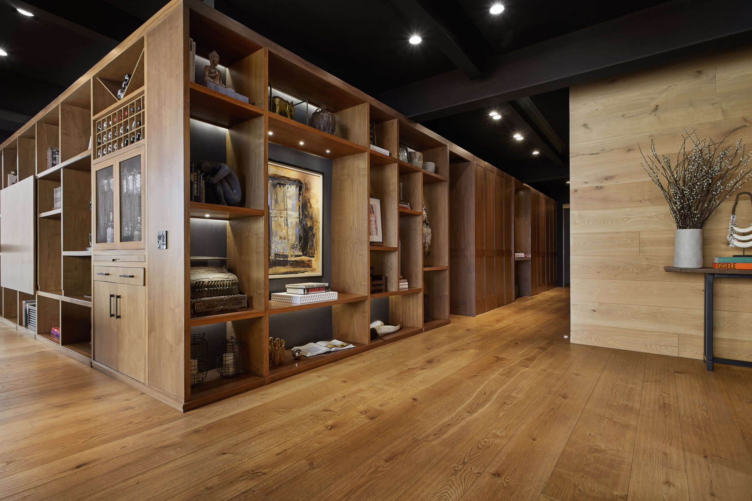 Estantería de madera con libros y decoraciones en una sala moderna con suelo de madera y paredes de madera clara.