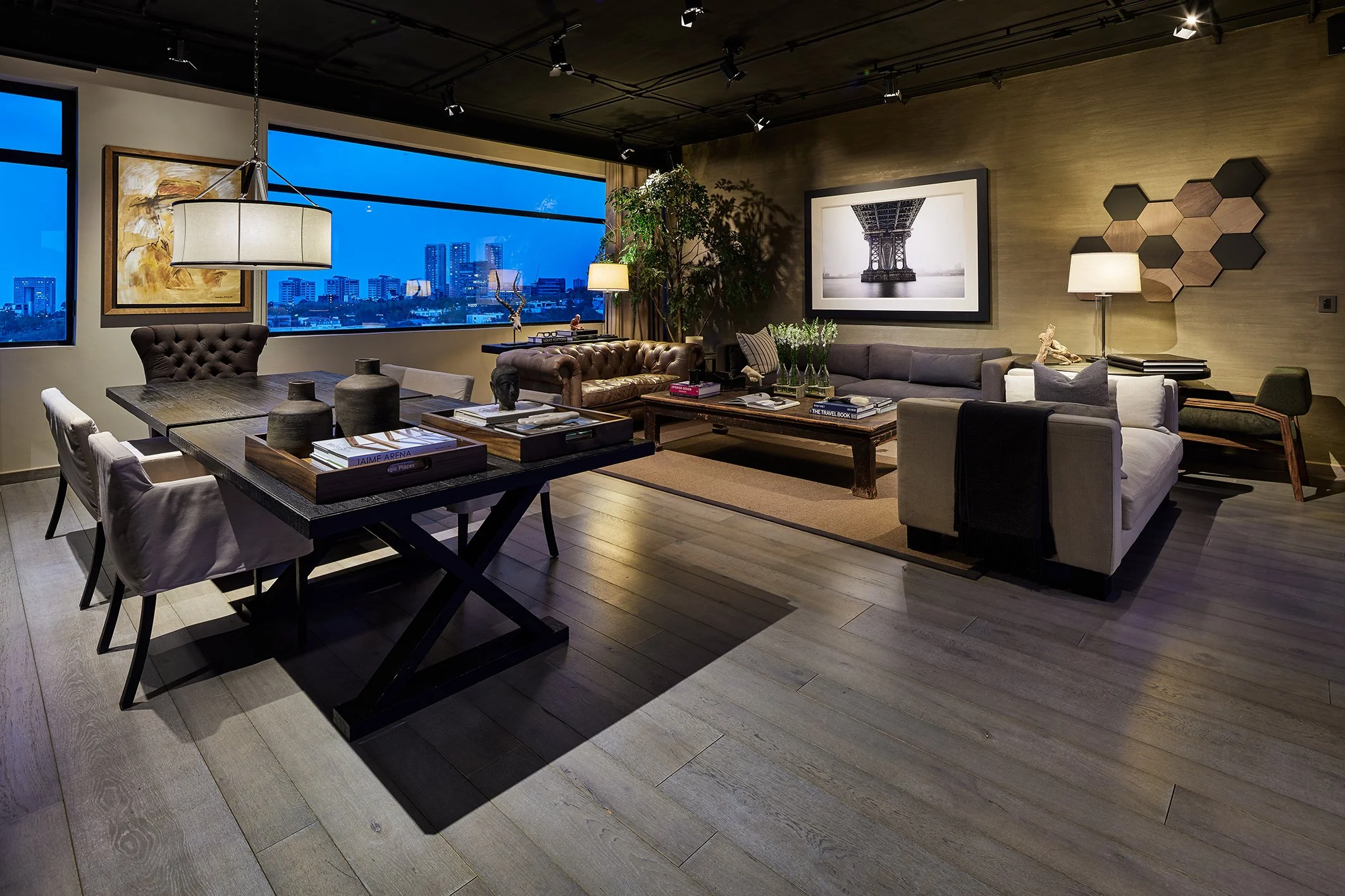 Sala moderna y elegante con sillones, mesa de centro, cuadros y lámparas, vista de ciudad a través de ventanas grandes.