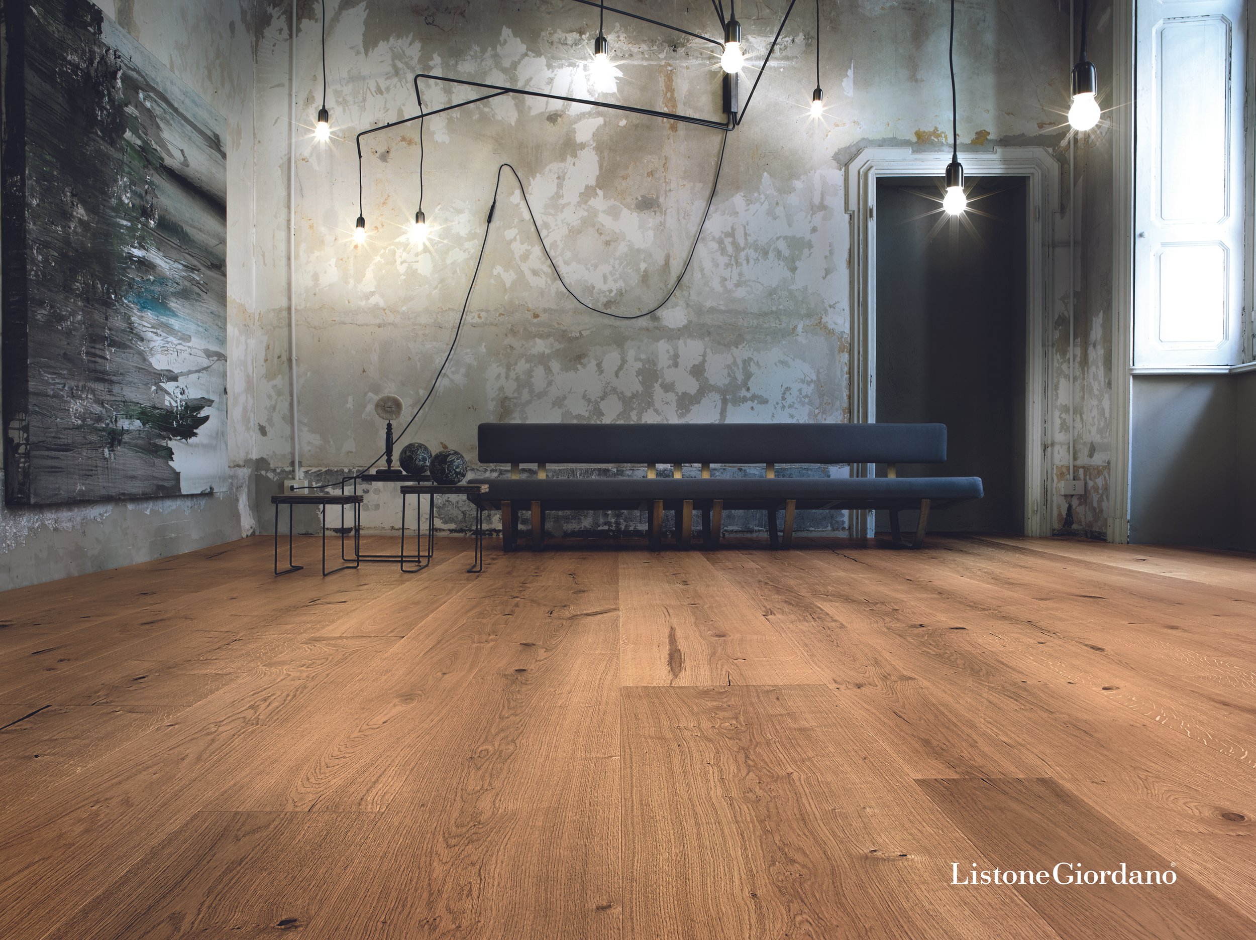 Interior minimalista con paredes desgastadas, lámparas colgantes y piso de madera natural, con ventanas que dejan entrar luz natural.