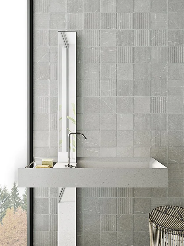 Tarja de lavabo moderna con espejo largo en un baño con paredes de azulejos grises.
