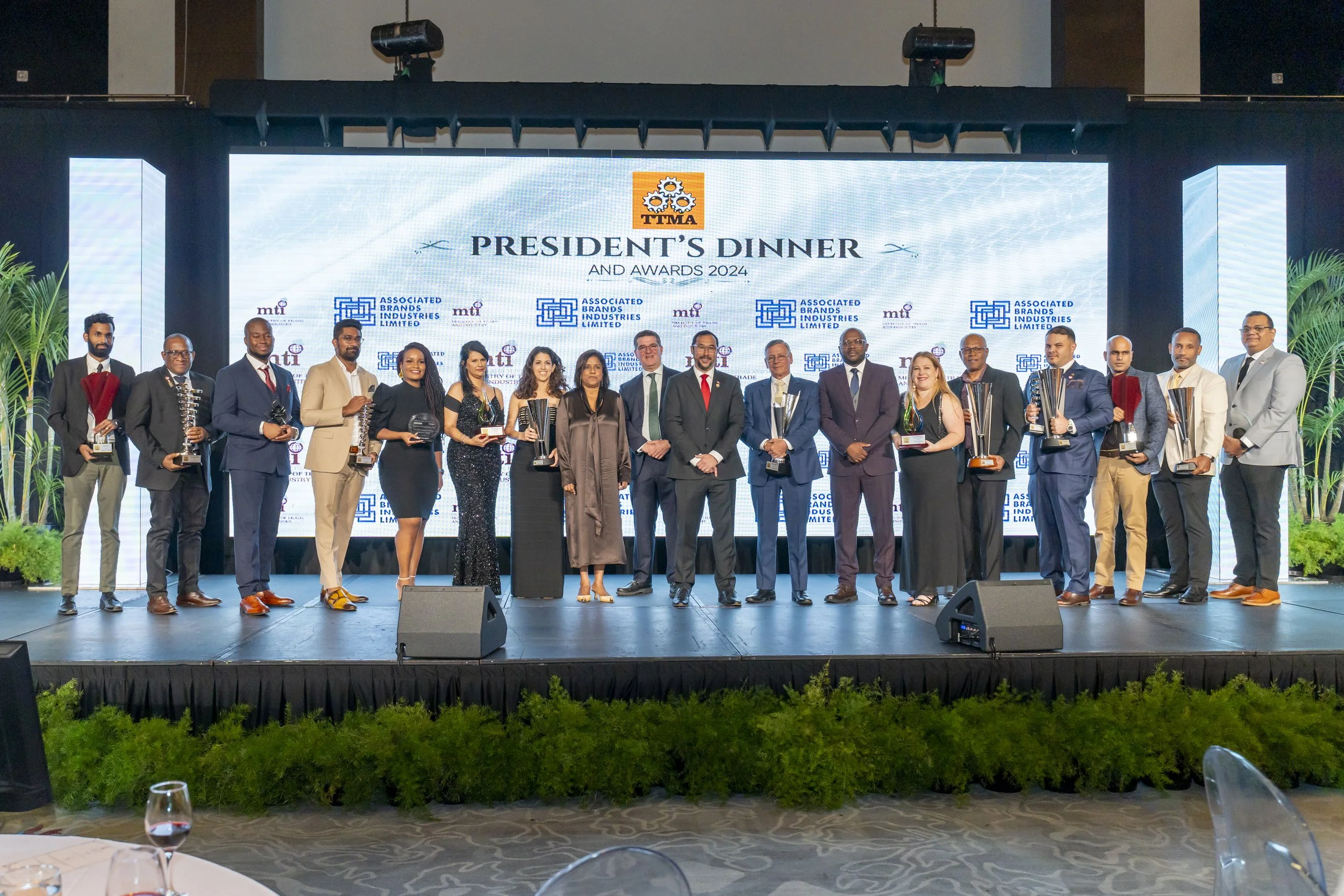 Group of people on stage at an awards ceremony with a large screen behind them displaying event details and logos.
