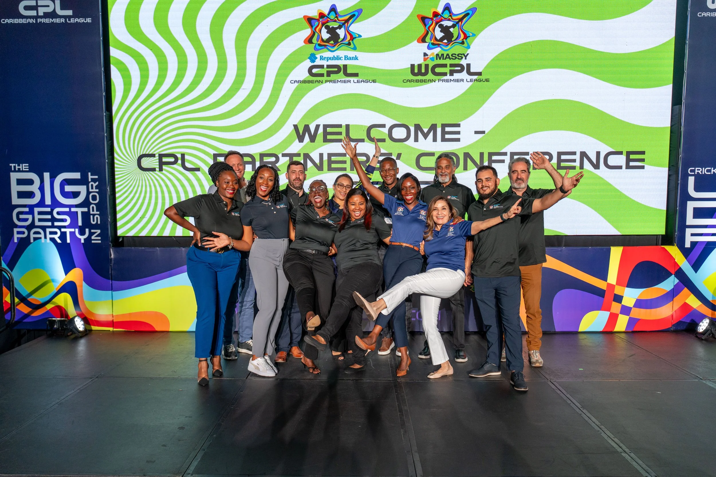 Group of smiling people standing in front of a colorful backdrop at the CPL Caribbean Premier League event, with a large sign that reads 'Welcome - CPL Partner Conference' in the background.