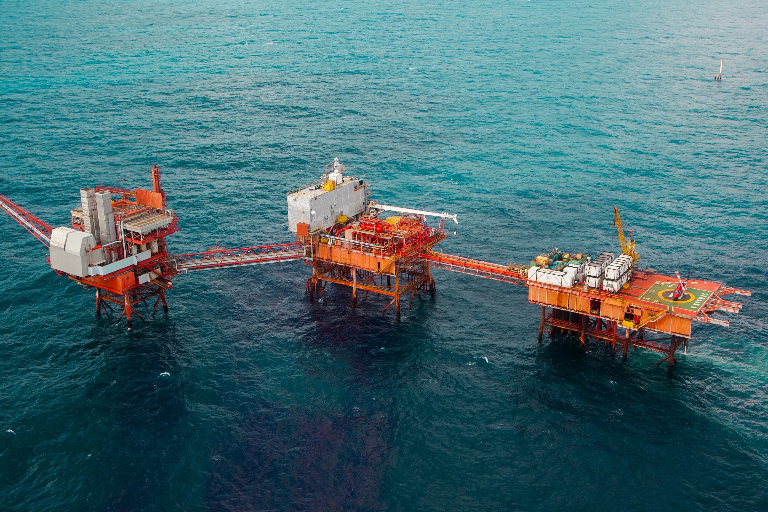 An offshore oil platform in the ocean with a helipad on the right side and equipment on top of the platform.