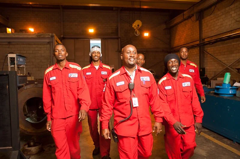Six people in red uniforms standing inside an industrial setting, smiling at the camera.