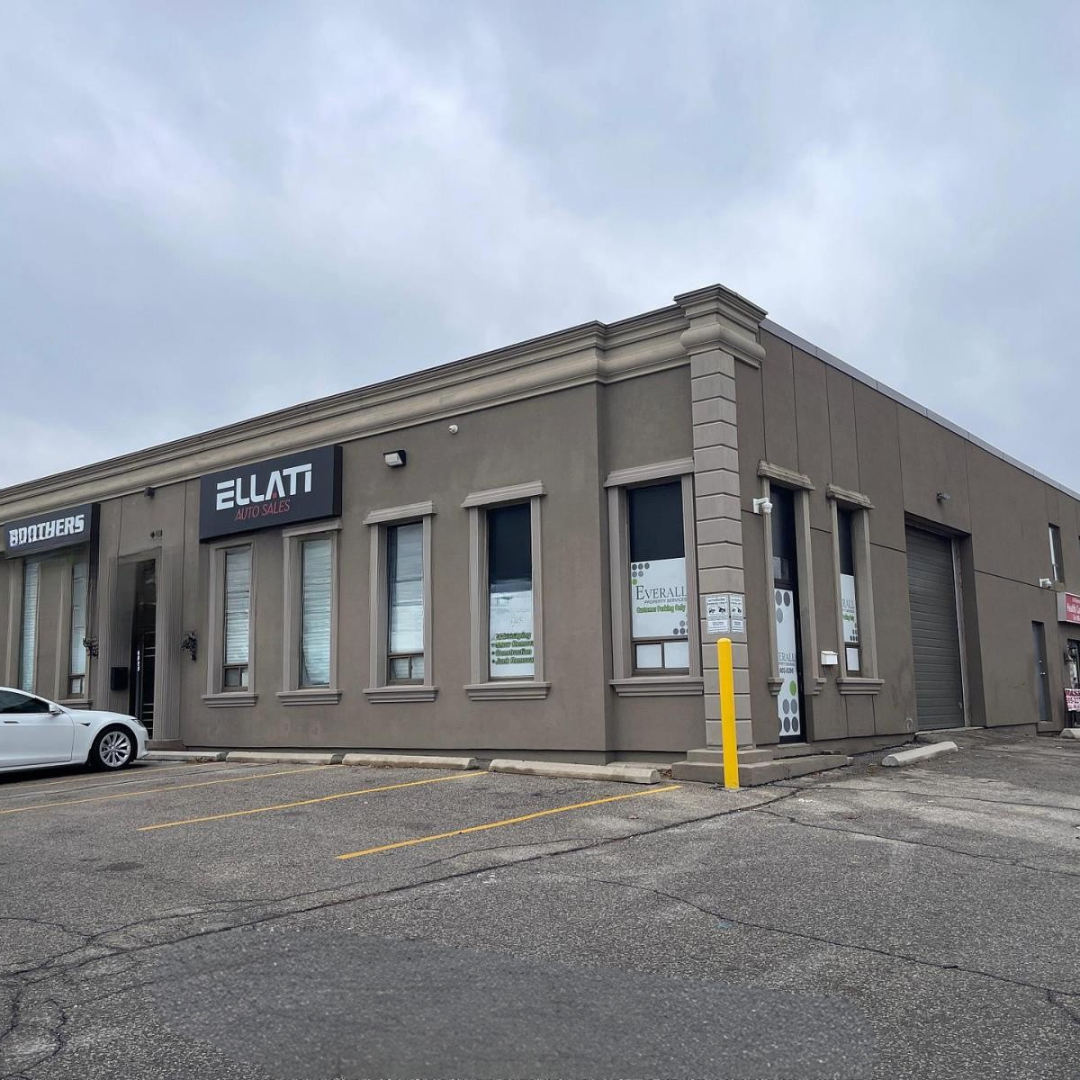 A commercial building with a gray exterior and several tall windows, with business signs.