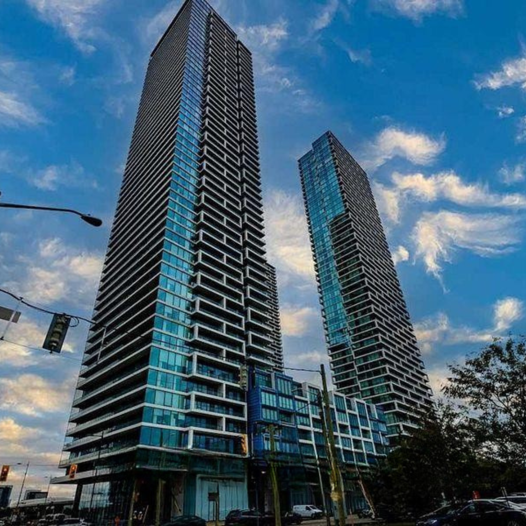 Two tall modern glass skyscrapers against a partly cloudy sky, with streetlights and cars in the foreground.