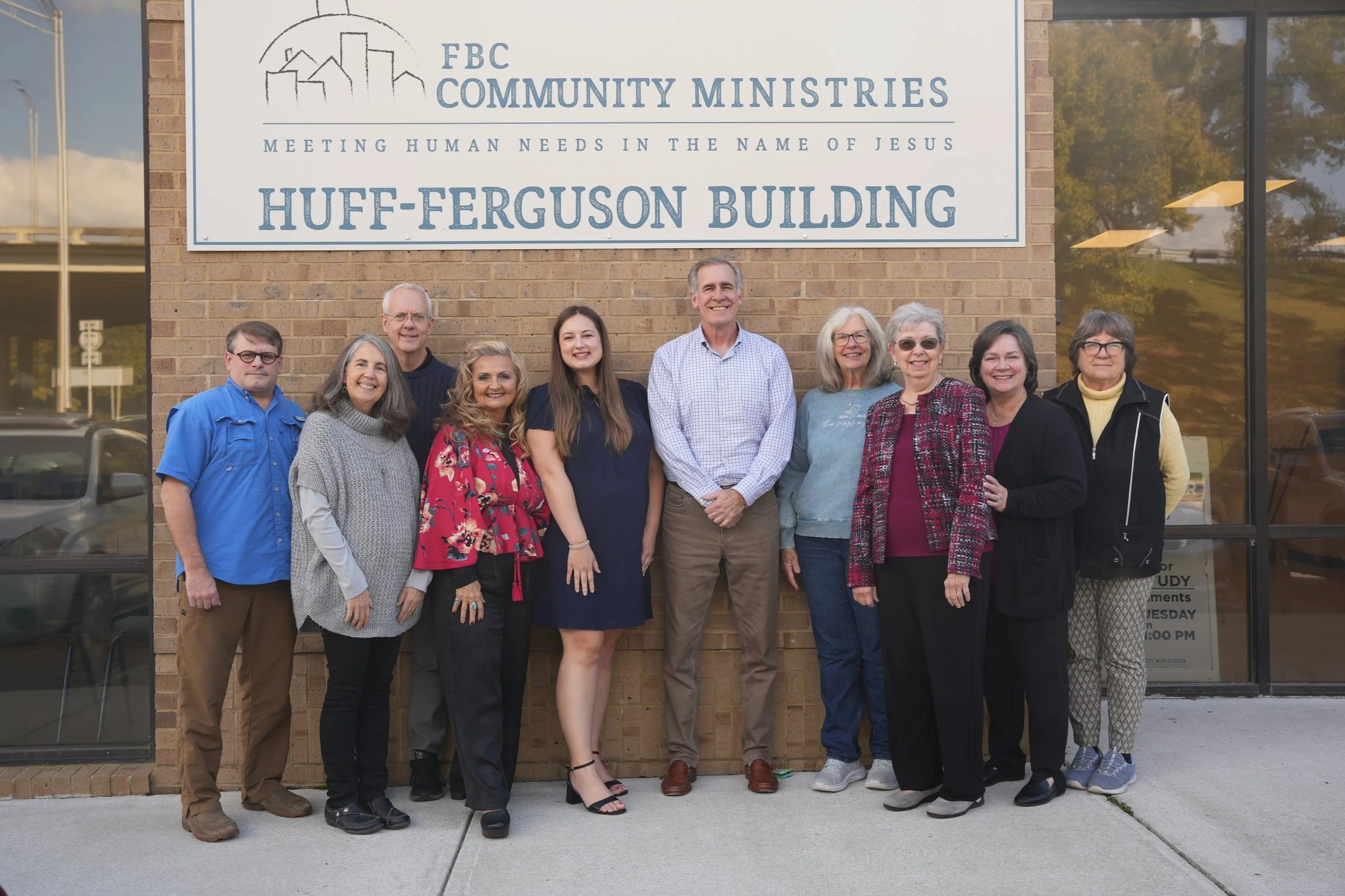 A group of twelve people standing in front of a brick building with a sign that reads 'FBC Community Ministries, Huff-Ferguson Building'.