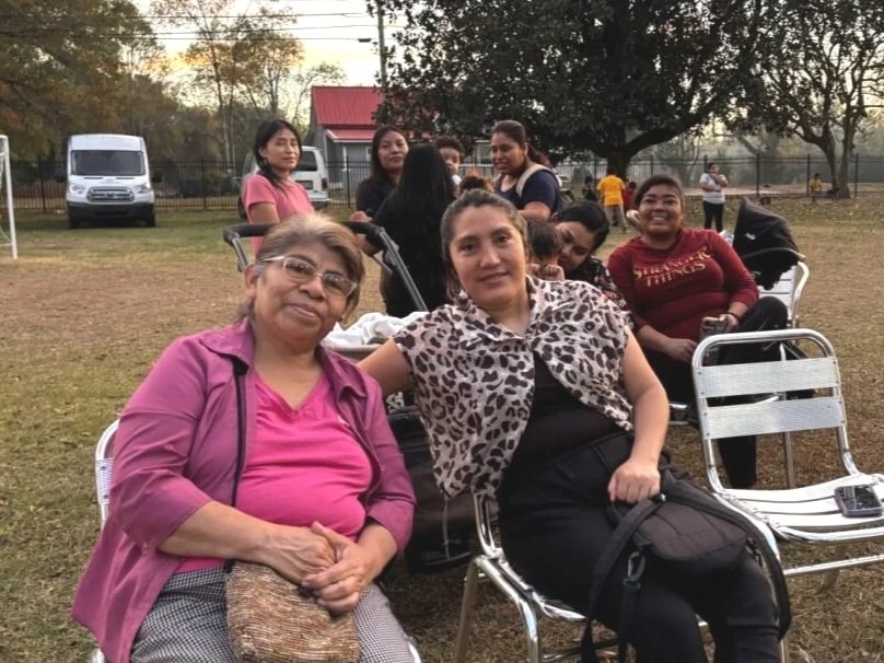 A landscape of a mountain range with snow-capped peaks, hills covered with grass and some modern buildings in the foreground.