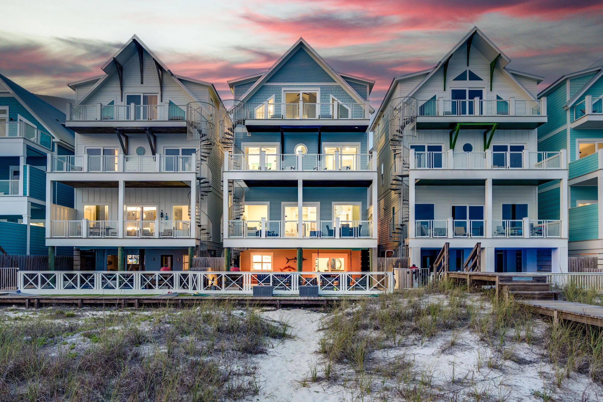 Multiple beach houses with outdoor balconies and spiral staircases, sand and grassy dunes in foreground, sunset sky in background - Real estate photography in 30A, Destin, and Panama City Beach by Matt Jozwiak