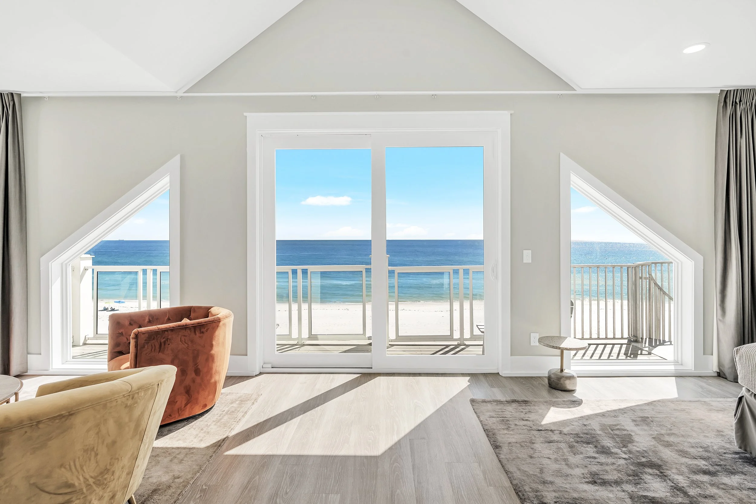Living room with large sliding glass doors leading to a balcony overlooking the ocean, with two small windows on sides, beige and brown furniture - Real estate photography in 30A, Destin, and Panama City Beach by Matt Jozwiak