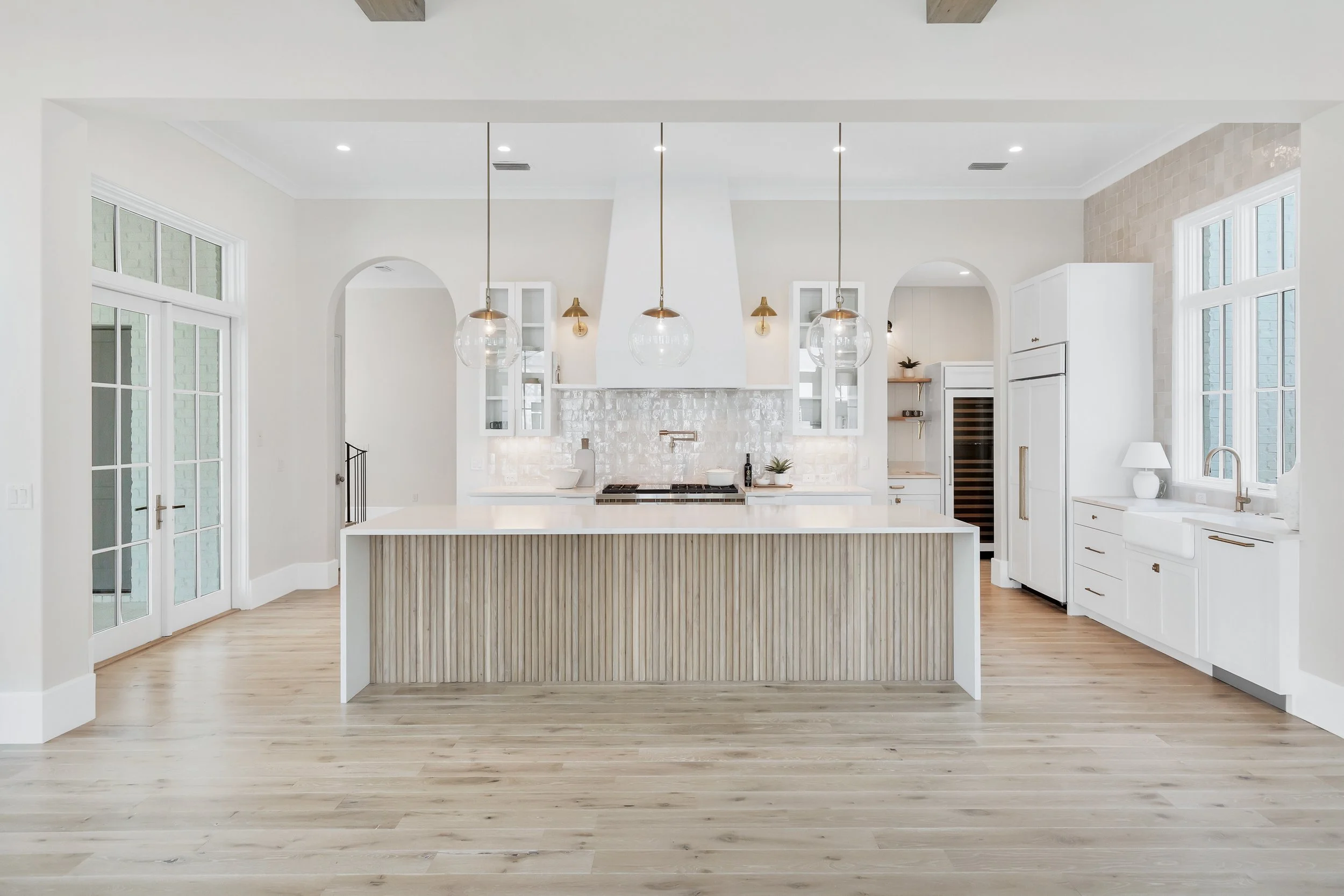 Modern white kitchen with large island, pendant lights, white cabinetry, and hardwood floors - Real estate photography in 30A, Destin, and Panama City Beach by Matt Jozwiak
