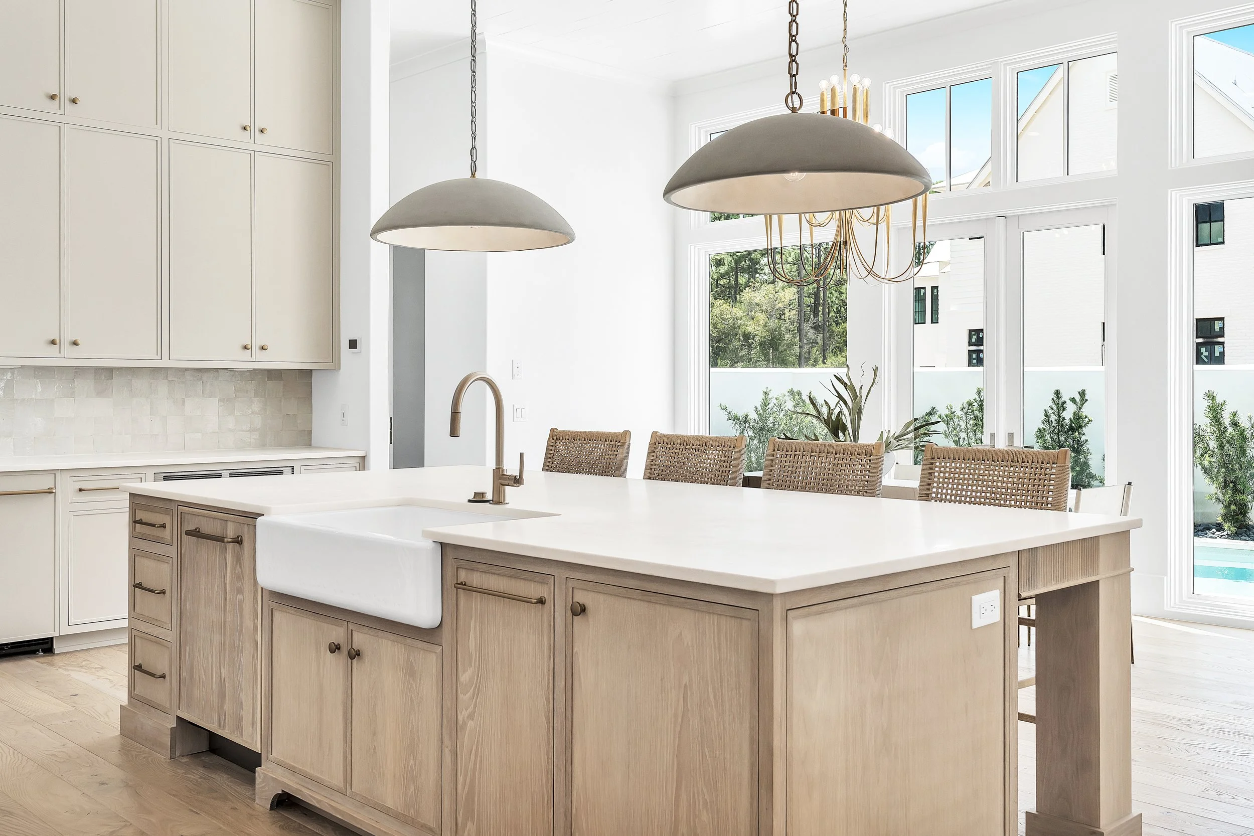 Modern kitchen with a large island, a farmhouse sink, beige cabinets, and large windows with a view of the outdoors - Real estate photography in 30A, Destin, and Panama City Beach by Matt Jozwiak
