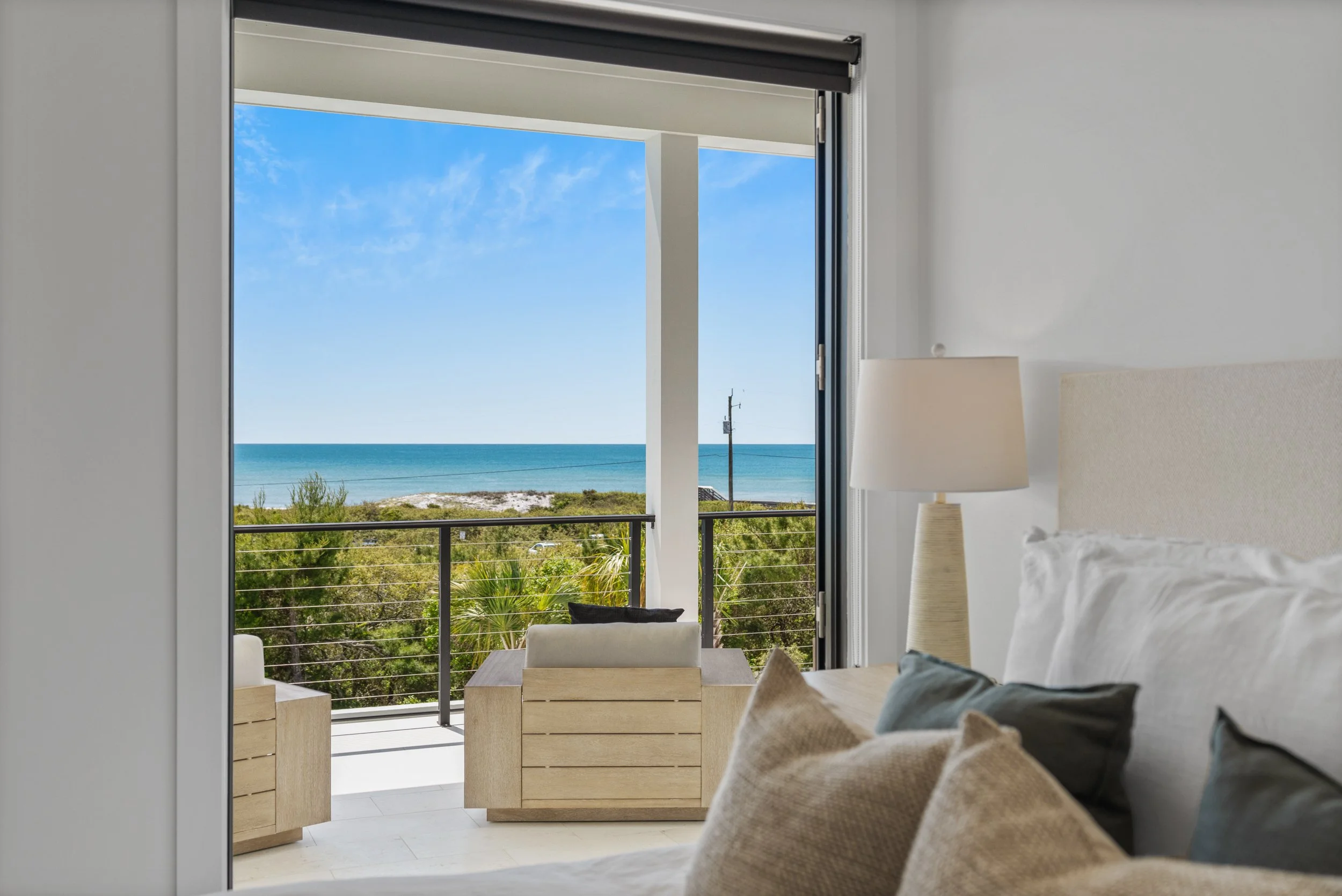 Bedroom with a view of the ocean, balcony with wooden chairs, and blue sky - Real estate photography in 30A, Destin, and Panama City Beach by Matt Jozwiak