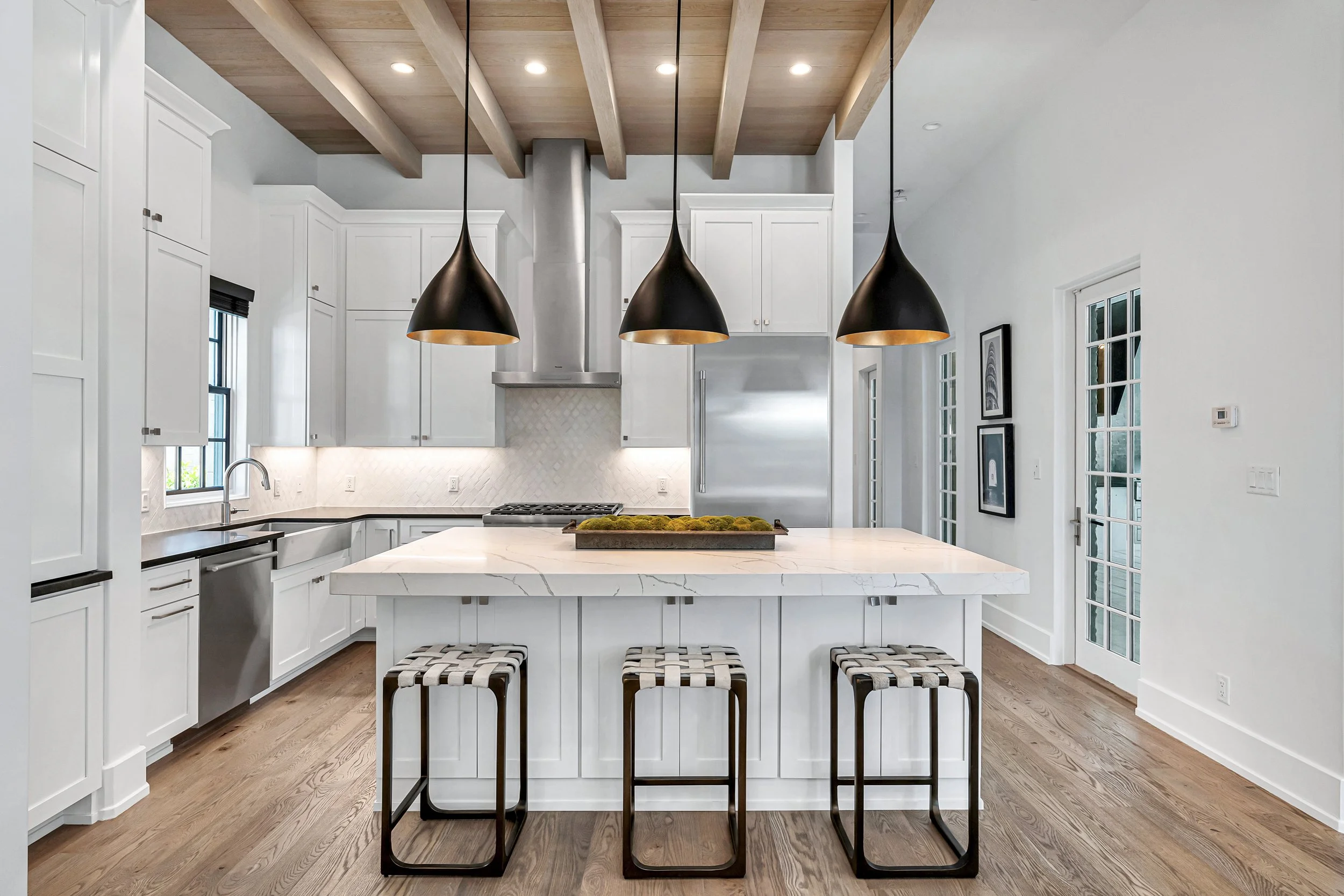 Modern kitchen with white cabinetry, a large marble island, black pendant lights, hardwood flooring, and a stainless steel refrigerator - Real estate photography in 30A, Destin, and Panama City Beach by Matt Jozwiak
