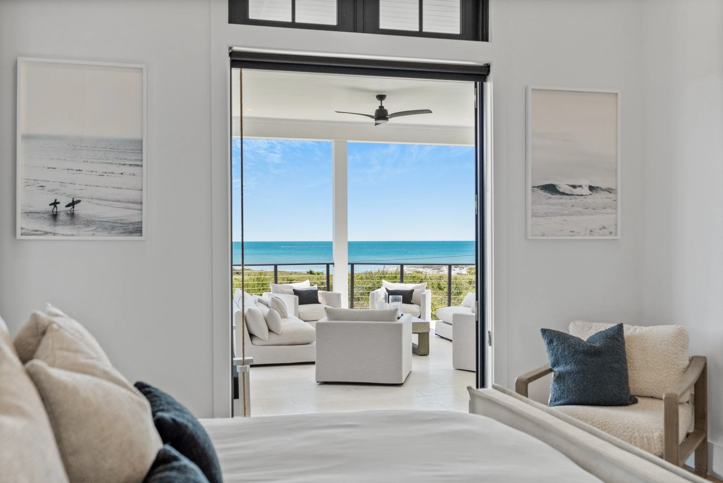 A bedroom with white walls and a bed in the foreground with beige and black pillows. Two framed black and white ocean-themed photographs are on the walls. - Real estate photography in 30A, Destin, and Panama City Beach by Matt Jozwiak