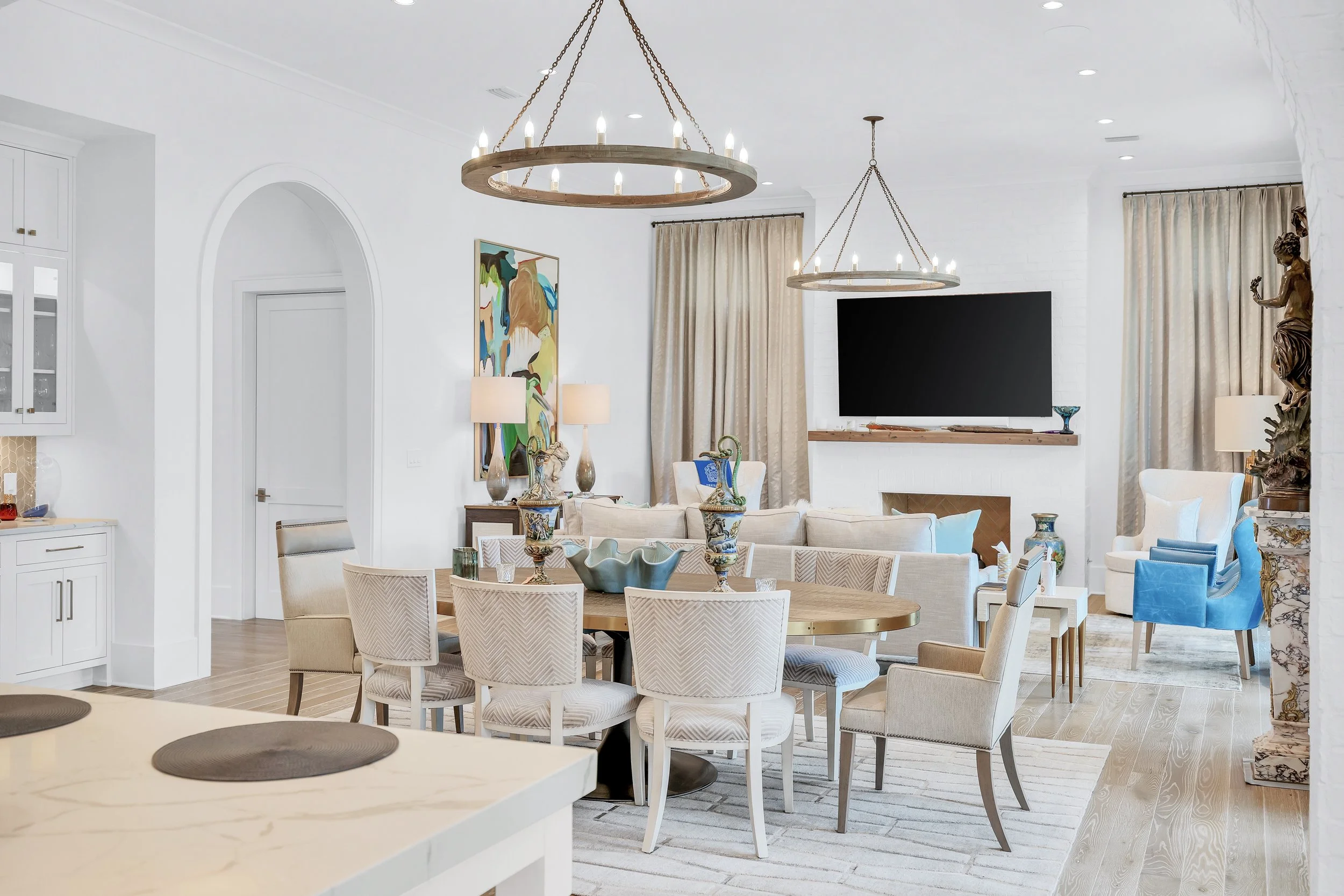Modern open-concept living and dining room with white walls, light wood flooring, round dining table with beige chairs, blue armchairs - Real estate photography in 30A, Destin, and Panama City Beach by Matt Jozwiak