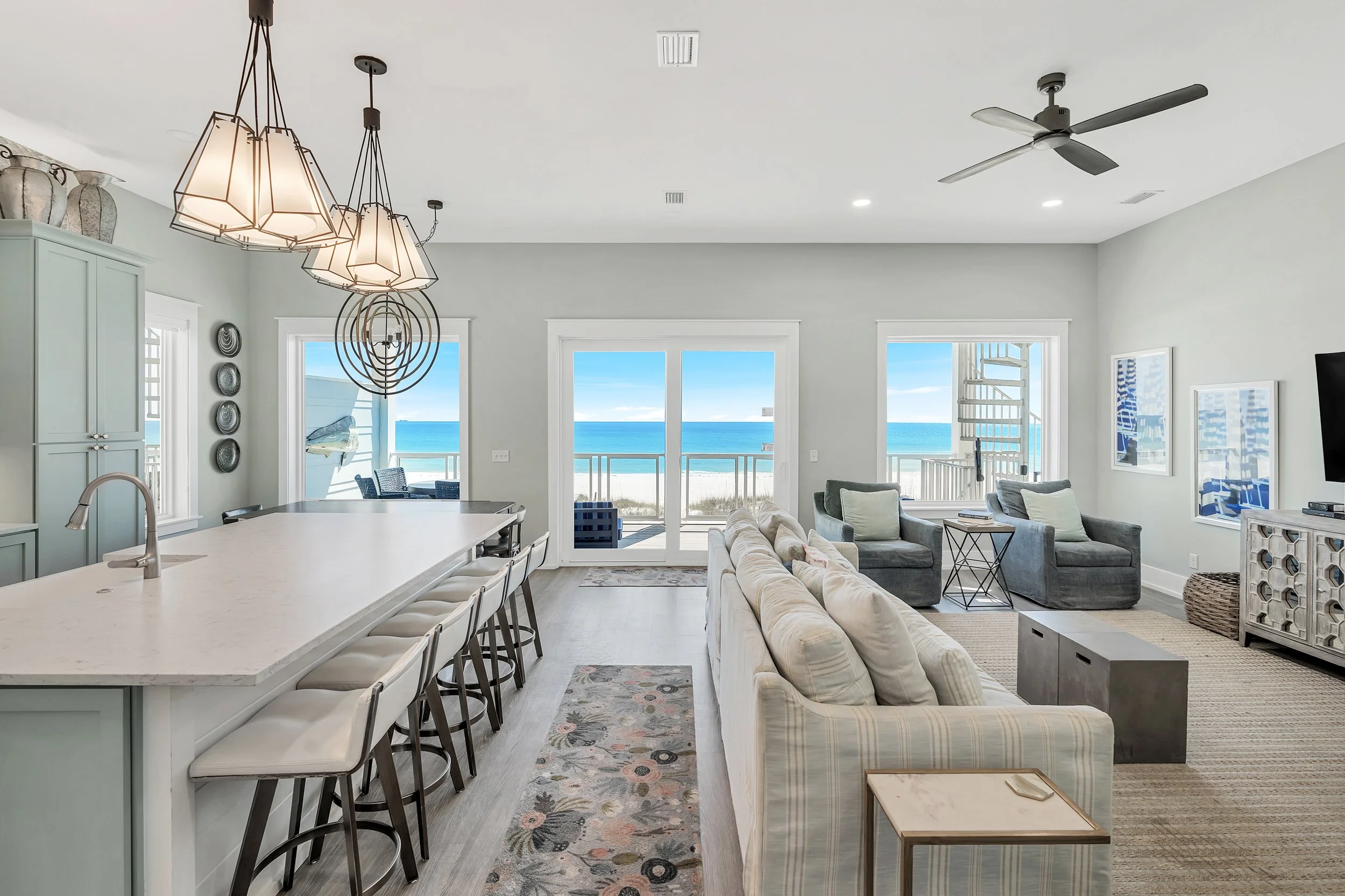 Bright open-concept living room and kitchen with ocean view, featuring a large island with white countertop, pendant lights, a sofa, two armchairs - Real estate photography in 30A, Destin, and Panama City Beach by Matt Jozwiak