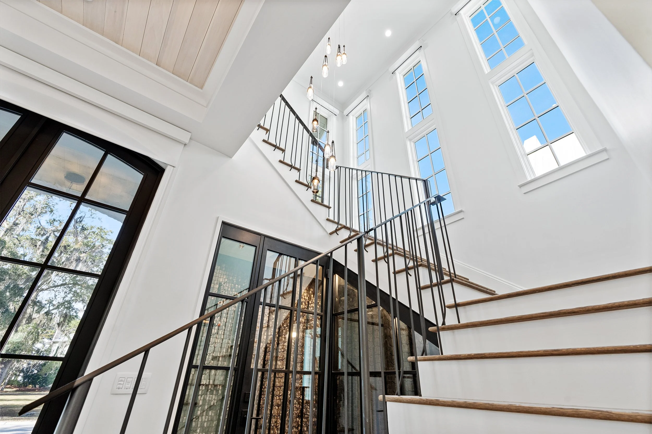 Modern interior staircase with black metal railings, wooden steps, large windows, and hanging light fixtures - Real estate photography in 30A, Destin, and Panama City Beach by Matt Jozwiak