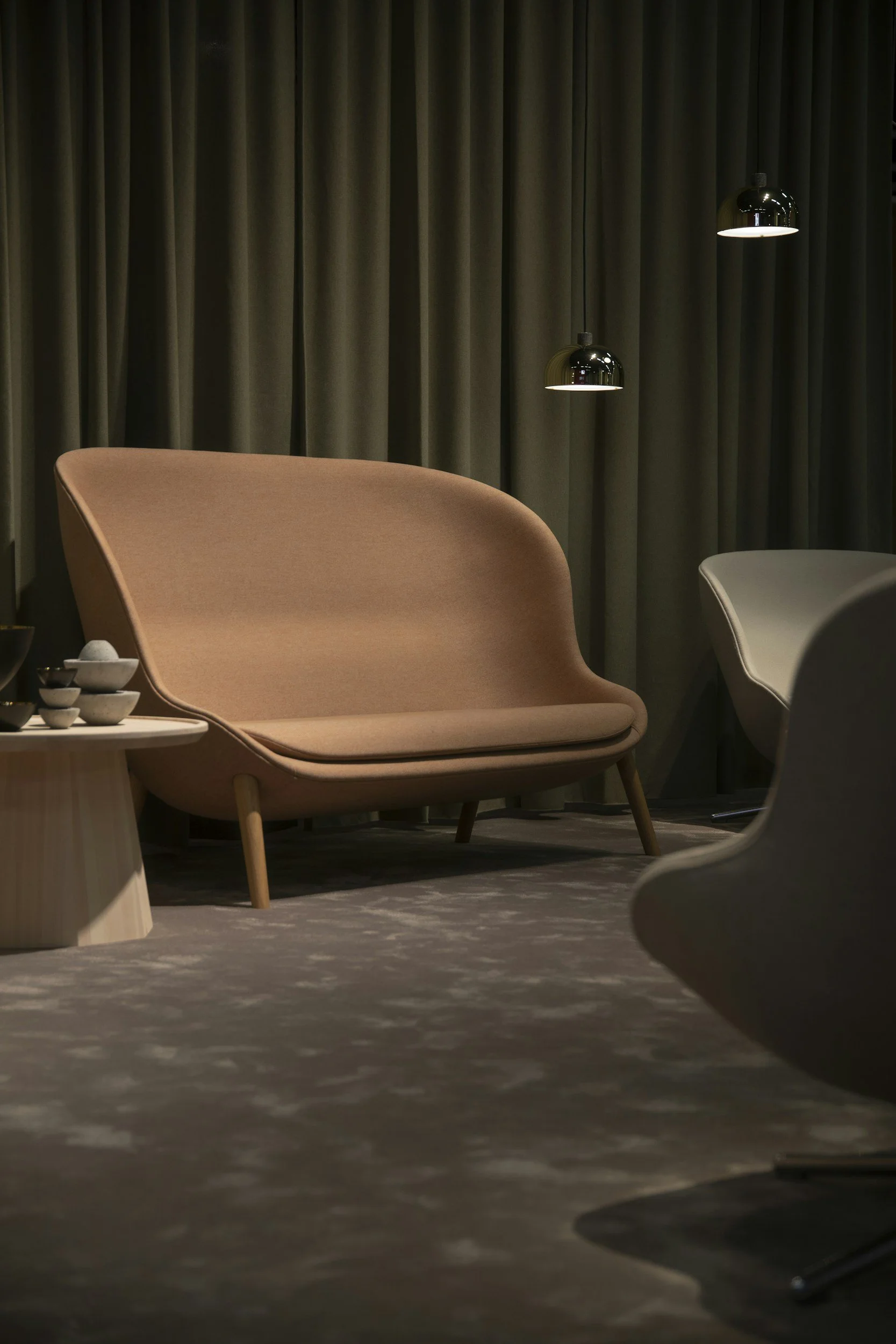 Soggiorno con divano rosa e altre sedie, tavolino con ciotole, tende scure e lampade nere appese al soffitto.