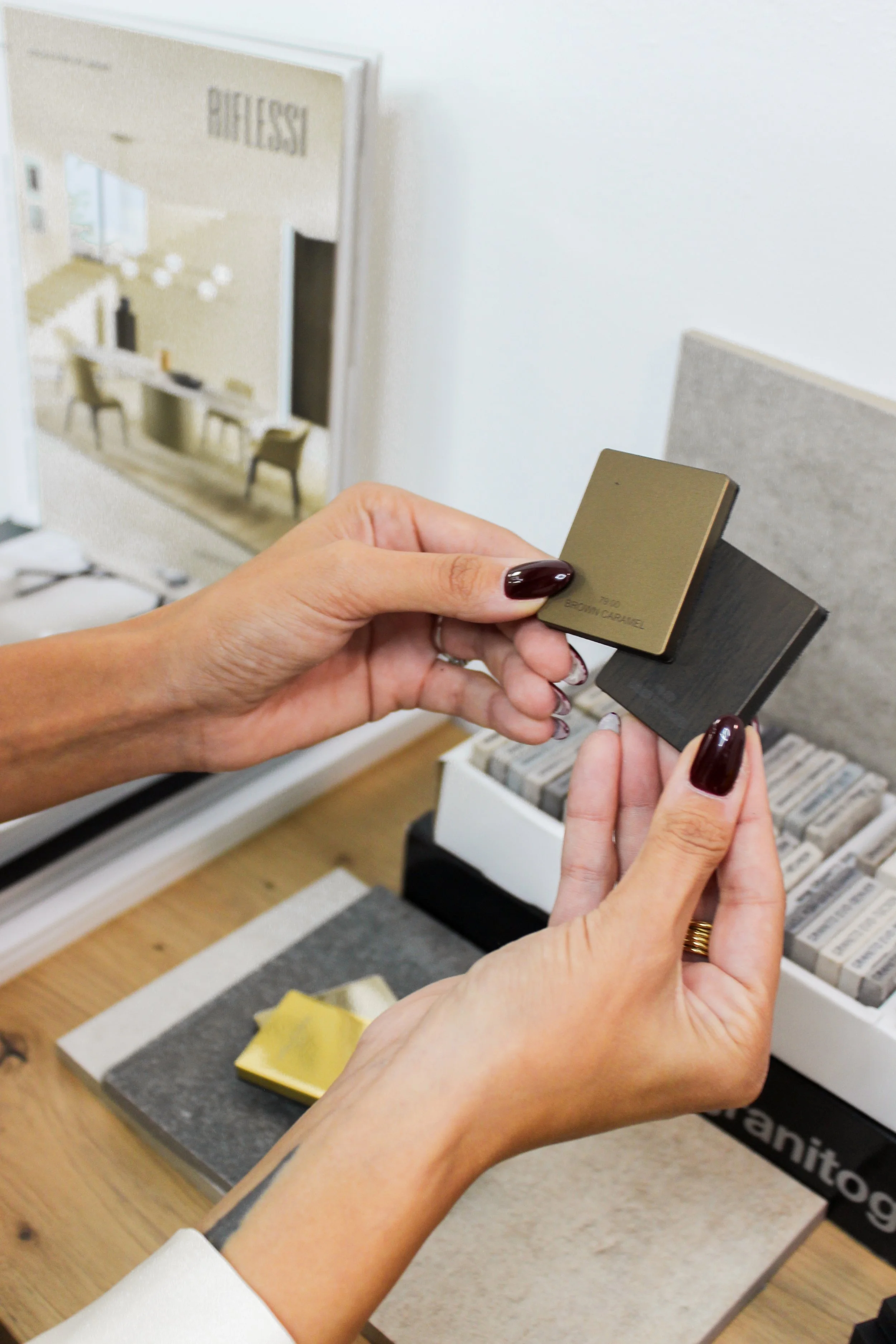 Due mani con smalto color bordeaux tengono due campioni di colore, uno beige e uno nero, in un negozio di materiali e finiture d'interni.