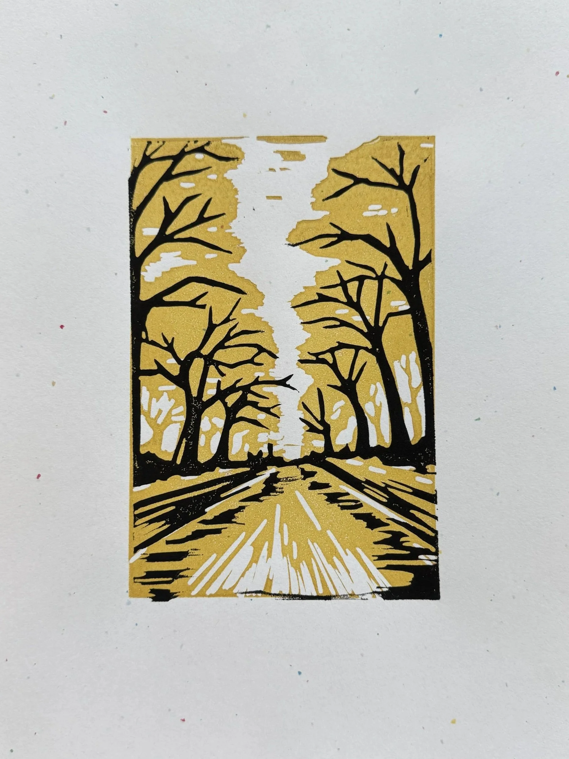 A black and gold paper cutout artwork depicting a pathway through a forest with leafless trees on both sides, with the pathway extending to the horizon.