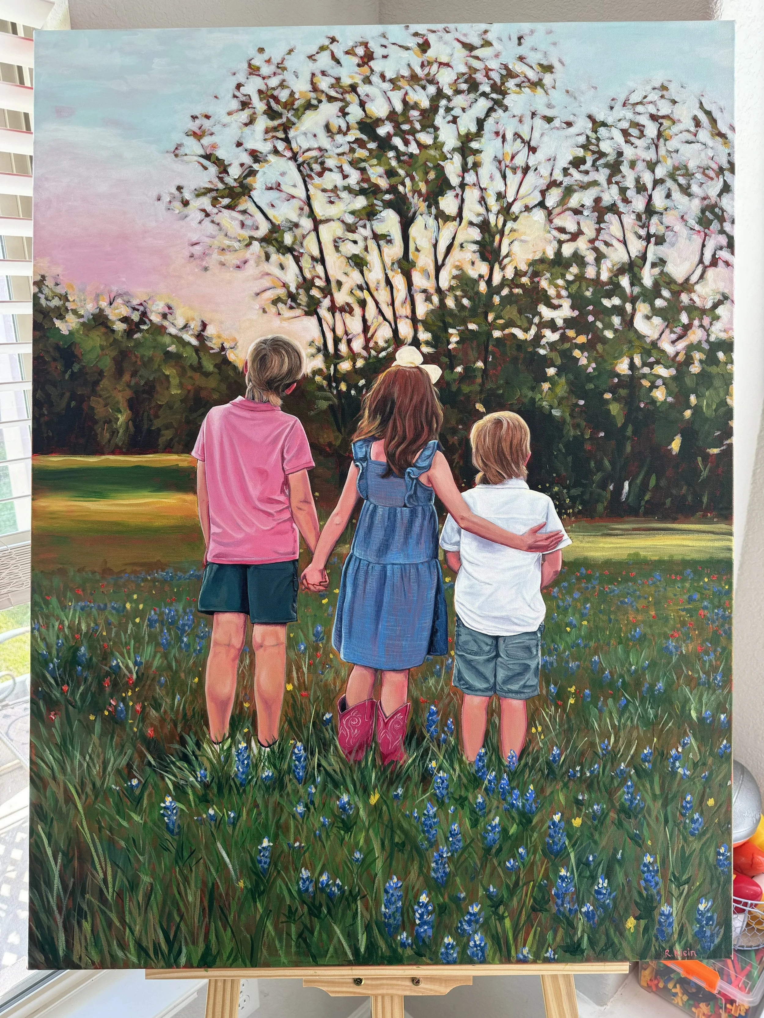 A painting of three children holding hands in a field of wildflowers, with a large blooming tree in the background during sunset.