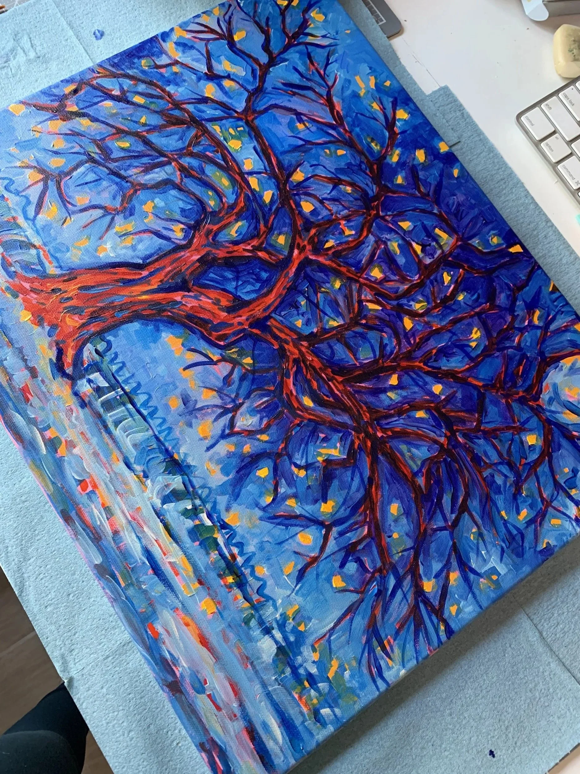 A painting of a tree with many branches on a blue background, featuring yellow leaves and red outlines, placed on a table.