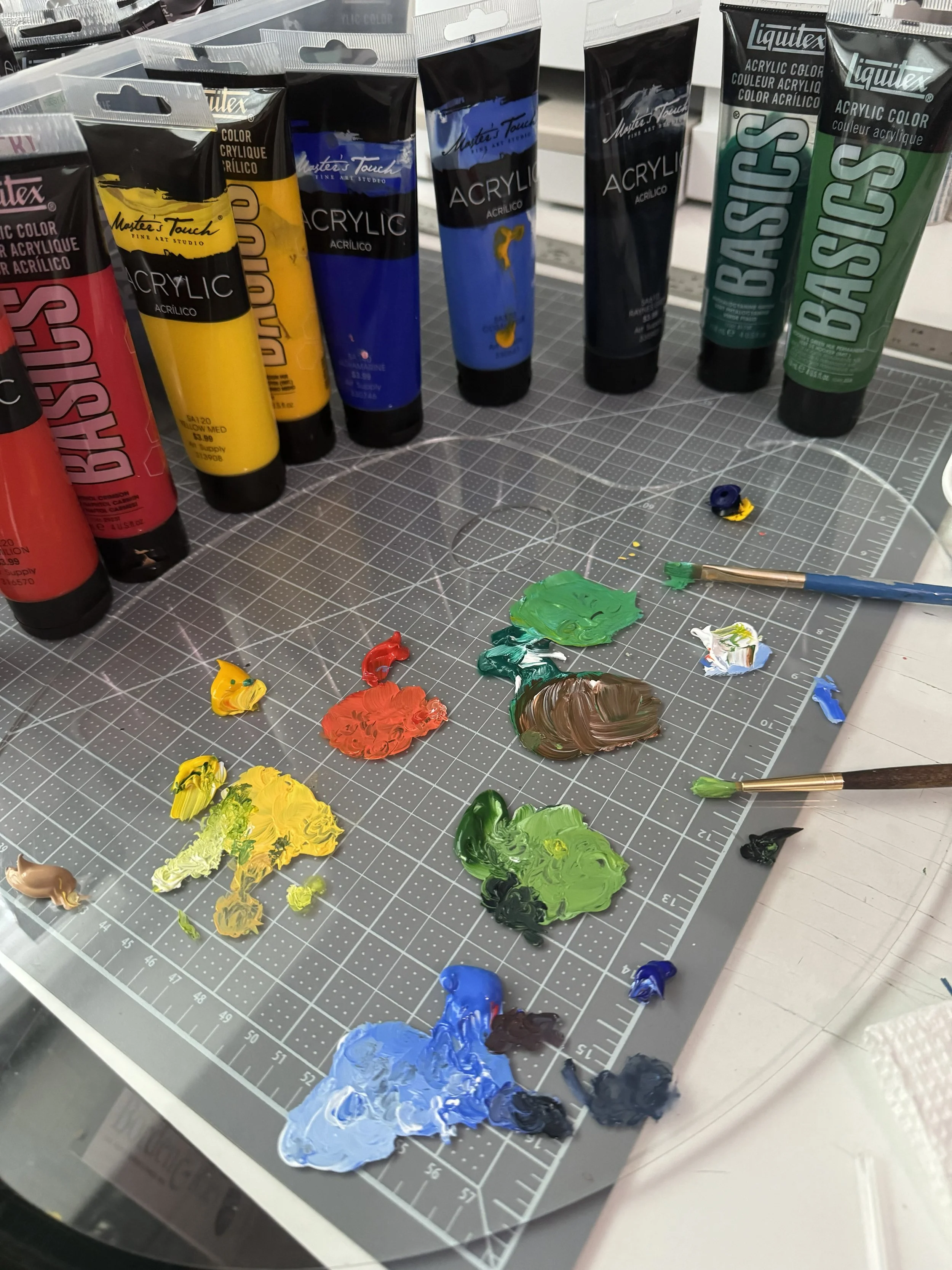 Assorted oil paints and paintbrushes on a gray cutting mat with paint smudges and color blobs.