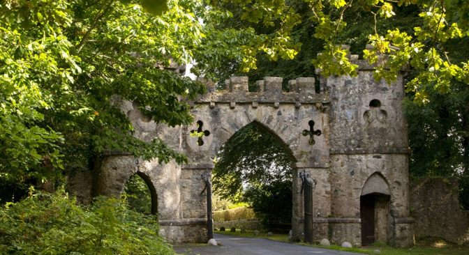 An old stone castle gate surrounded by green trees and foliage.