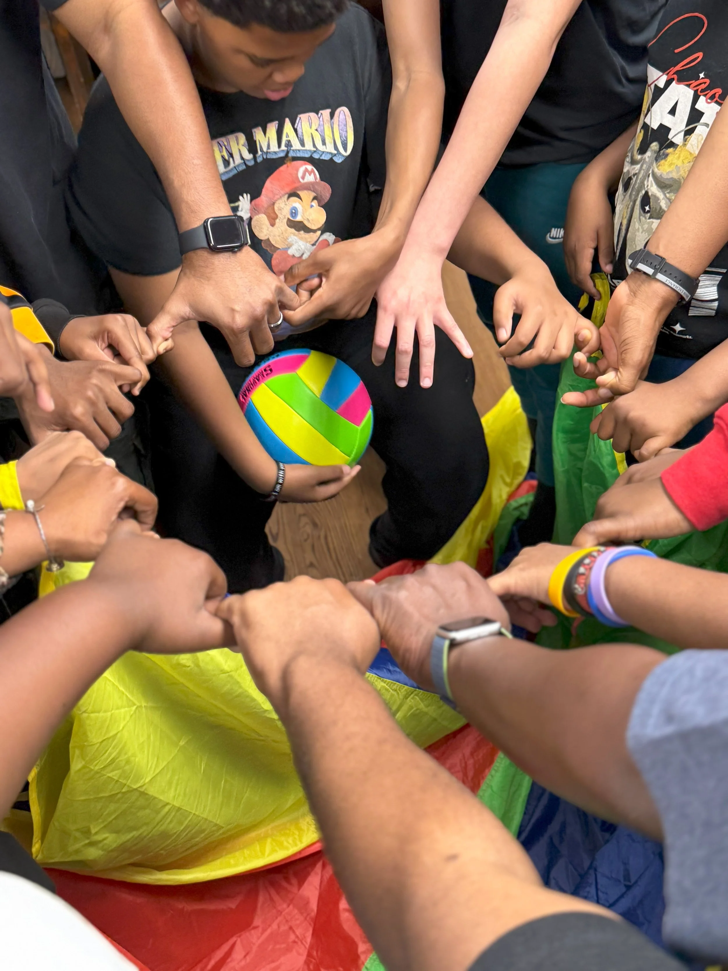 Group of children with diverse skin tones gathered in a circle, holding a colorful beach ball, participating in a team activity.