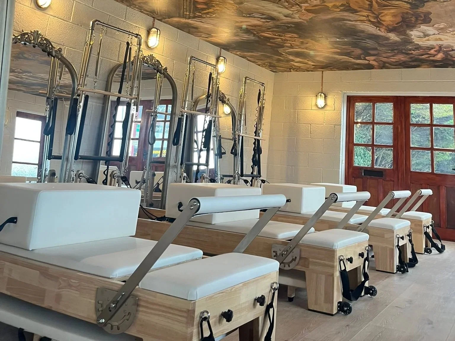 Reformer Pilates equipment arranged in a bright studio with windows and wooden door