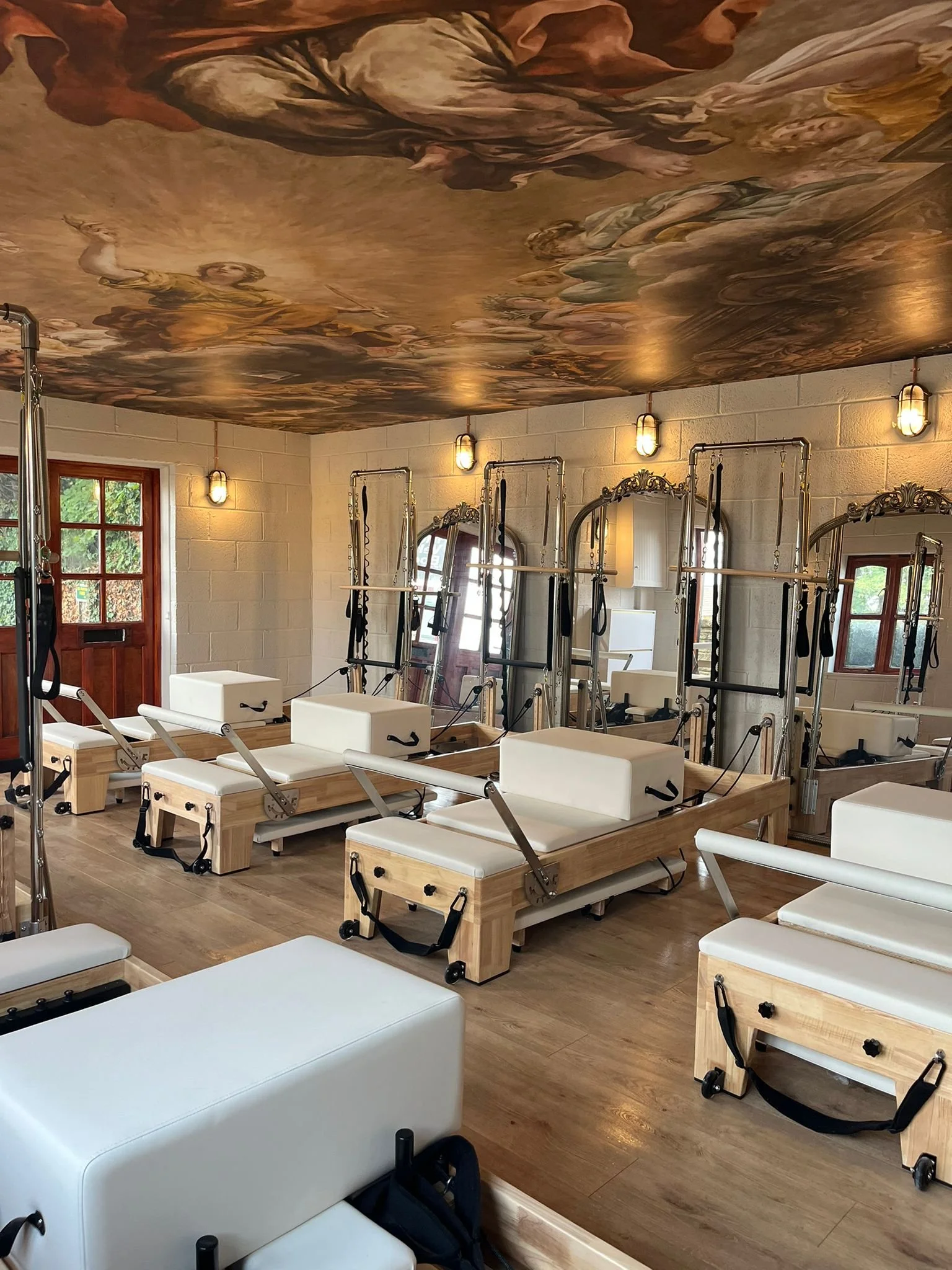 Pilates reformer machines in a yoga studio with a decorative painted ceiling and mirrors on the wall.