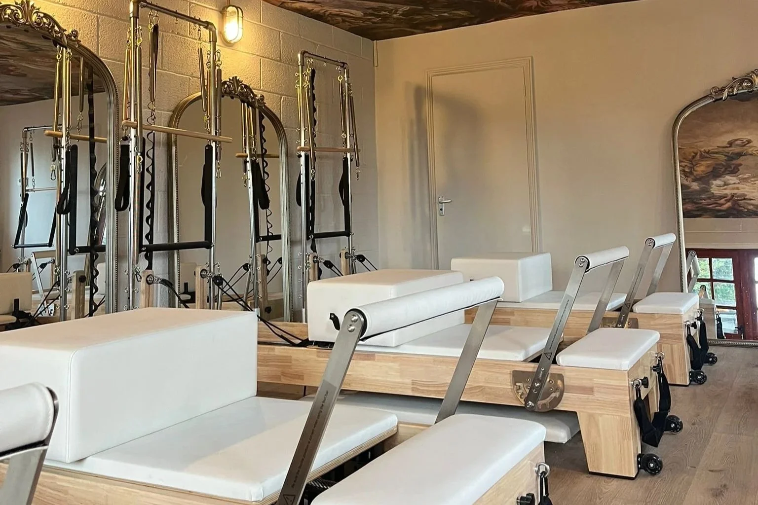 Pilates reformer machines with adjustable headers, straps, and pulleys in a fitness studio, with a mirror and a door in the background.