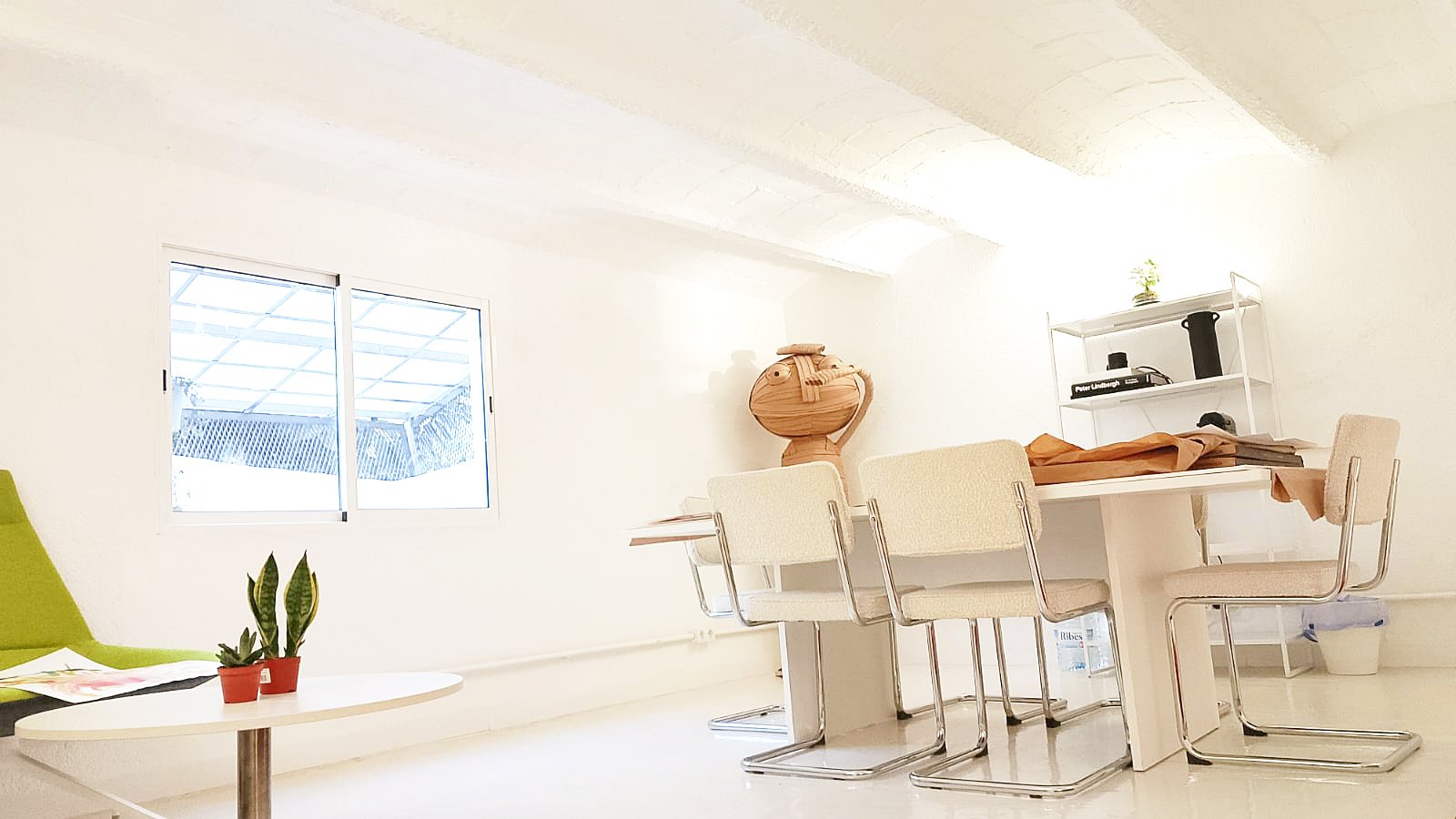 Sala de reuniones con mesa blanca, seis sillas beige, estantería blanca, ventana y decoración minimalista.