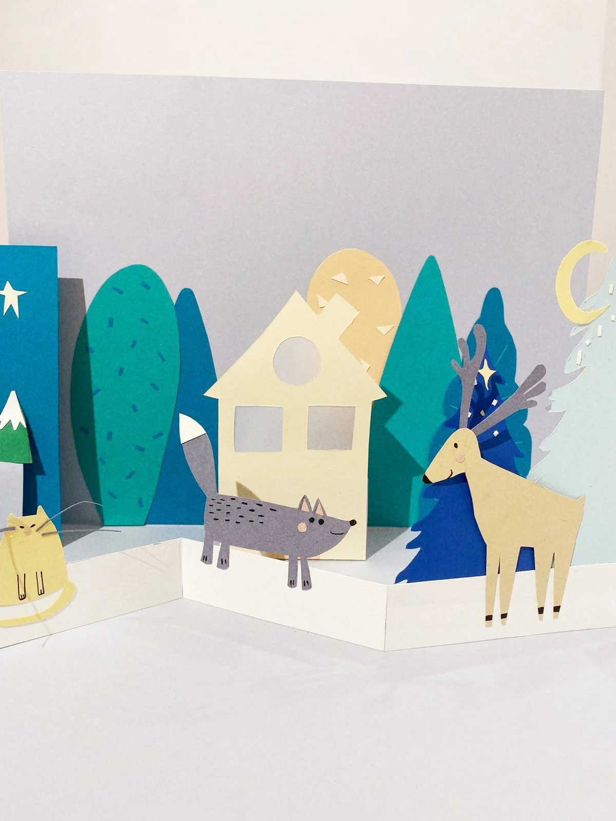 Escena en papel con animales y árboles en un entorno de bosque, incluyendo un ciervo, un lobo y un gato, con una casa en el centro.